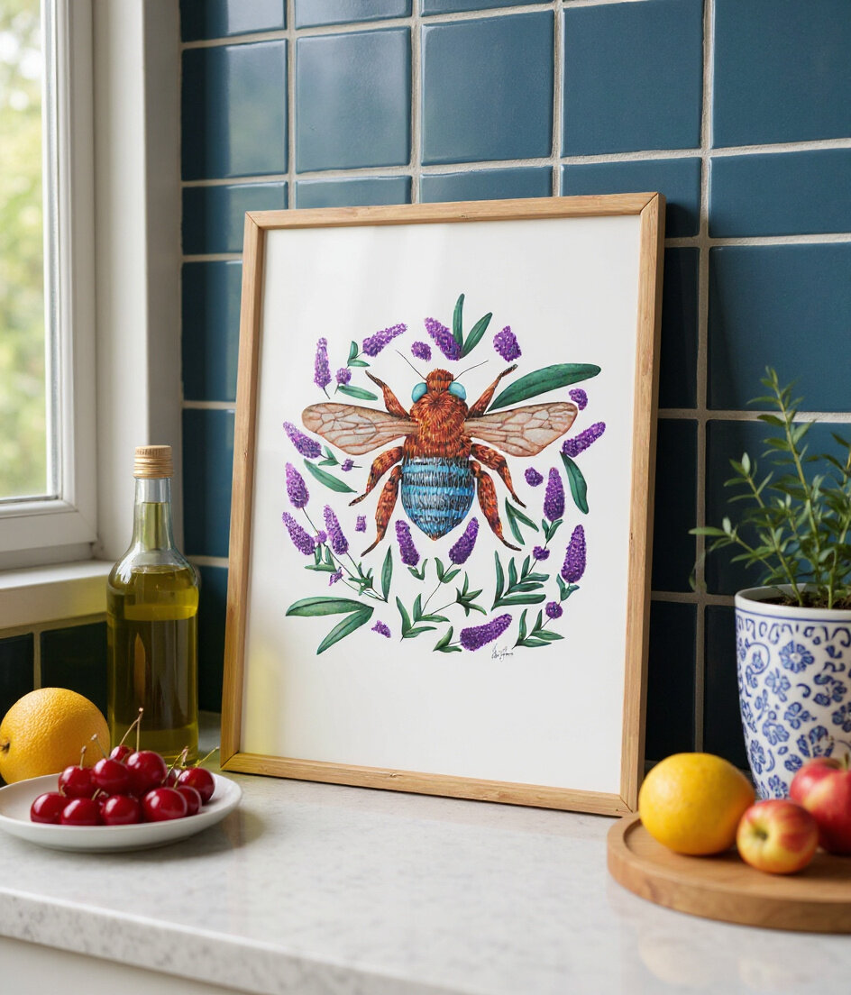 Framed illustration of a detailed bee surrounded by lavender sprigs, displayed on a kitchen bench next to fruit, olive oil, and plants