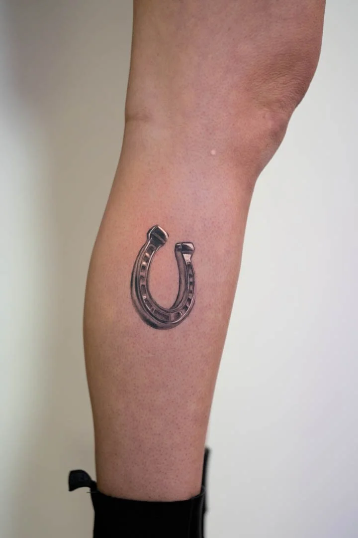 Healed realistic horse shoe tattoo on the outer right calf. Style is realistic black and grey chrome effect
