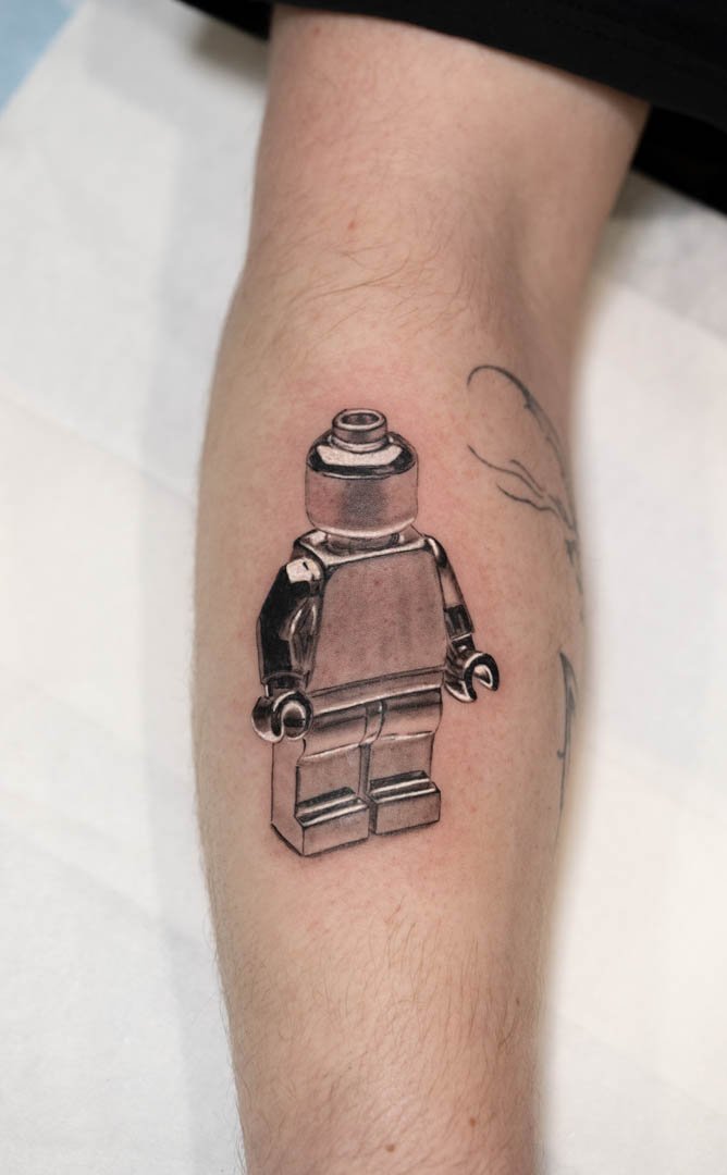 Realistic tattoo of a chrome lego man. Placement is outer left forearm. Style is realistic black and grey chrome effect