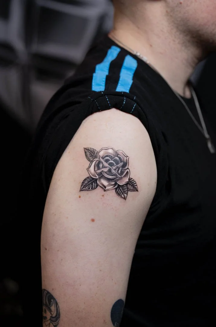 Traditional rose tattoo made to look chrome. Placement is on the upper arm at the cap of the shoulder. Style is black and grey realism / chrome effect.