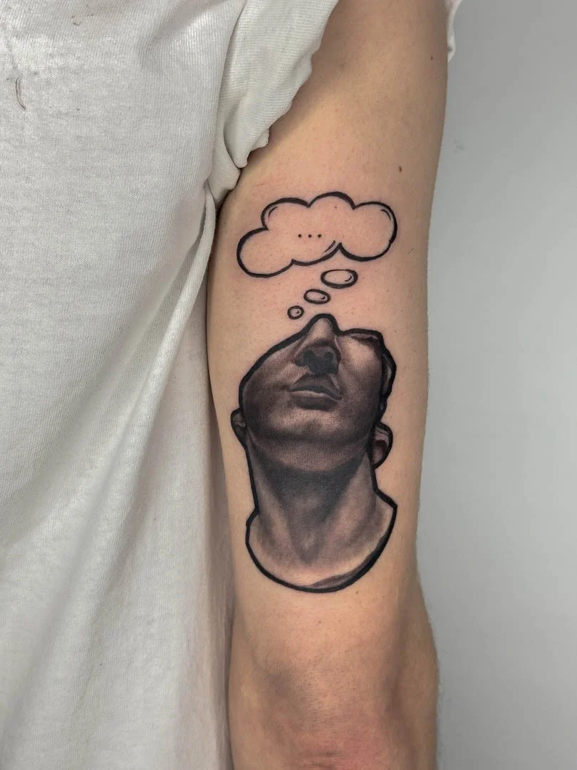 Greek bust statue with graphic thought bubble coming out from the top of the head. Placement is on the back of the right tricep. Style is soft black and grey with graphic elements.