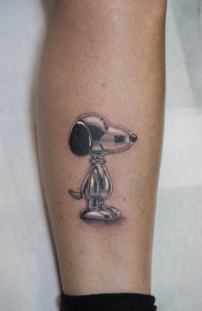 Photo showing an image of Peanuts character Snoopy as a metallic chrome statue. Placement is on the outer right calf. Style is realistic black and grey chrome effect