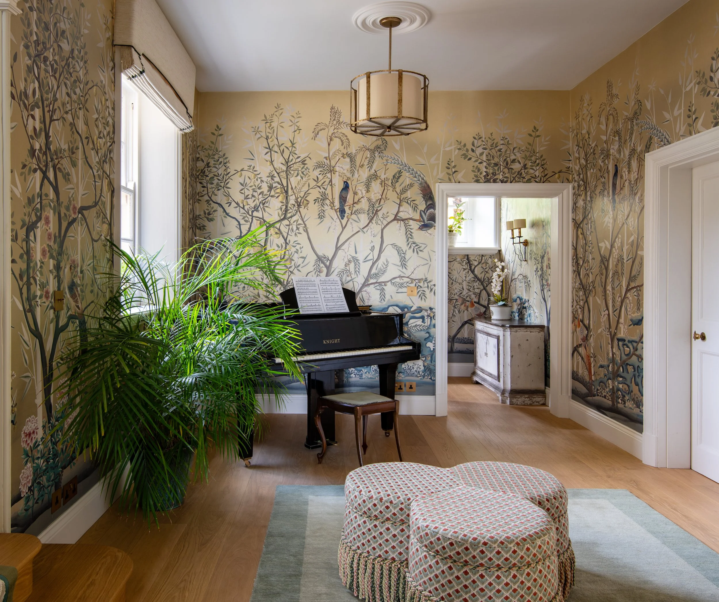 Music hall, designed by MIDA Interiors for a large Cotswolds country estate, featuring botanical mural wallpaper, a black piano, bespoke upholstery, oak flooring, tailored window dressing and contemporary statement lighting.