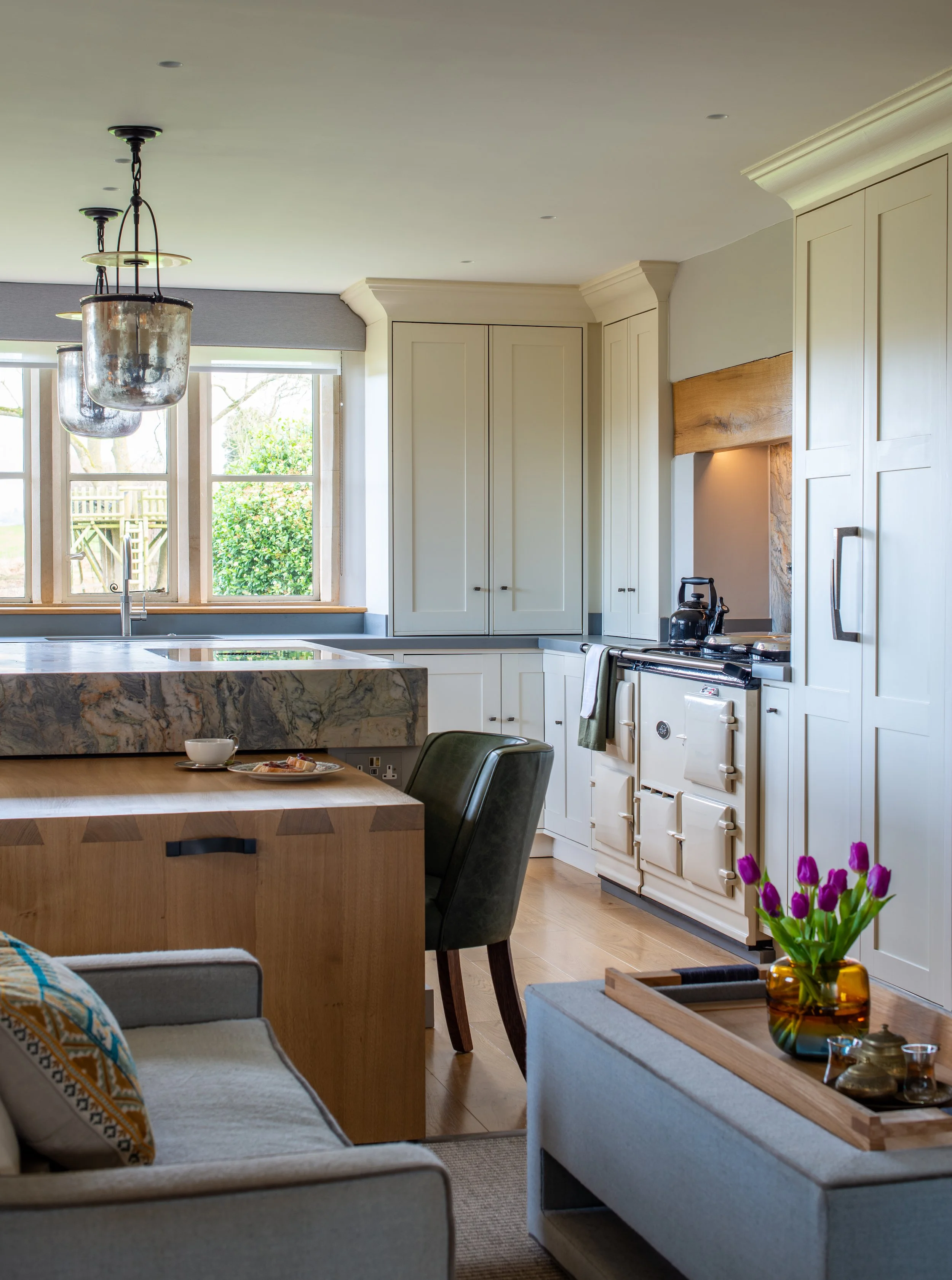 This portrait view shows the pull-out oak dining table integrated into the quartz waterfall island, with exposed dovetail joints expressing the quality of its construction. Bespoke full-height joinery reorganises storage around the AGA, while the new