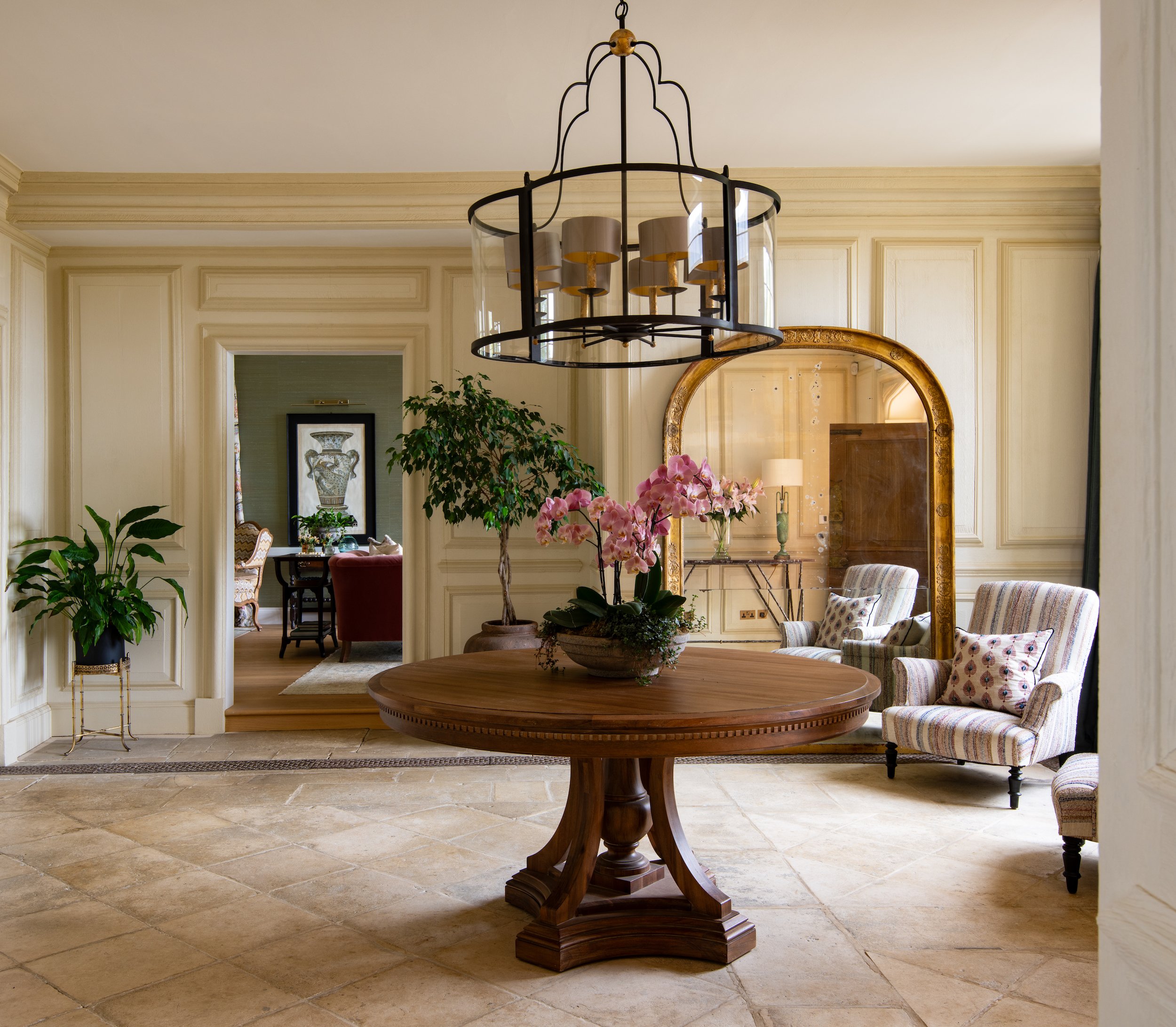 Grand entrance hall designed by MIDA Interiors for a large Cotswolds country estate, combining original wall panelling, antique furnishings, a statement lantern, original flag stone flooring and refined contemporary decoration for an elegant, eclecti