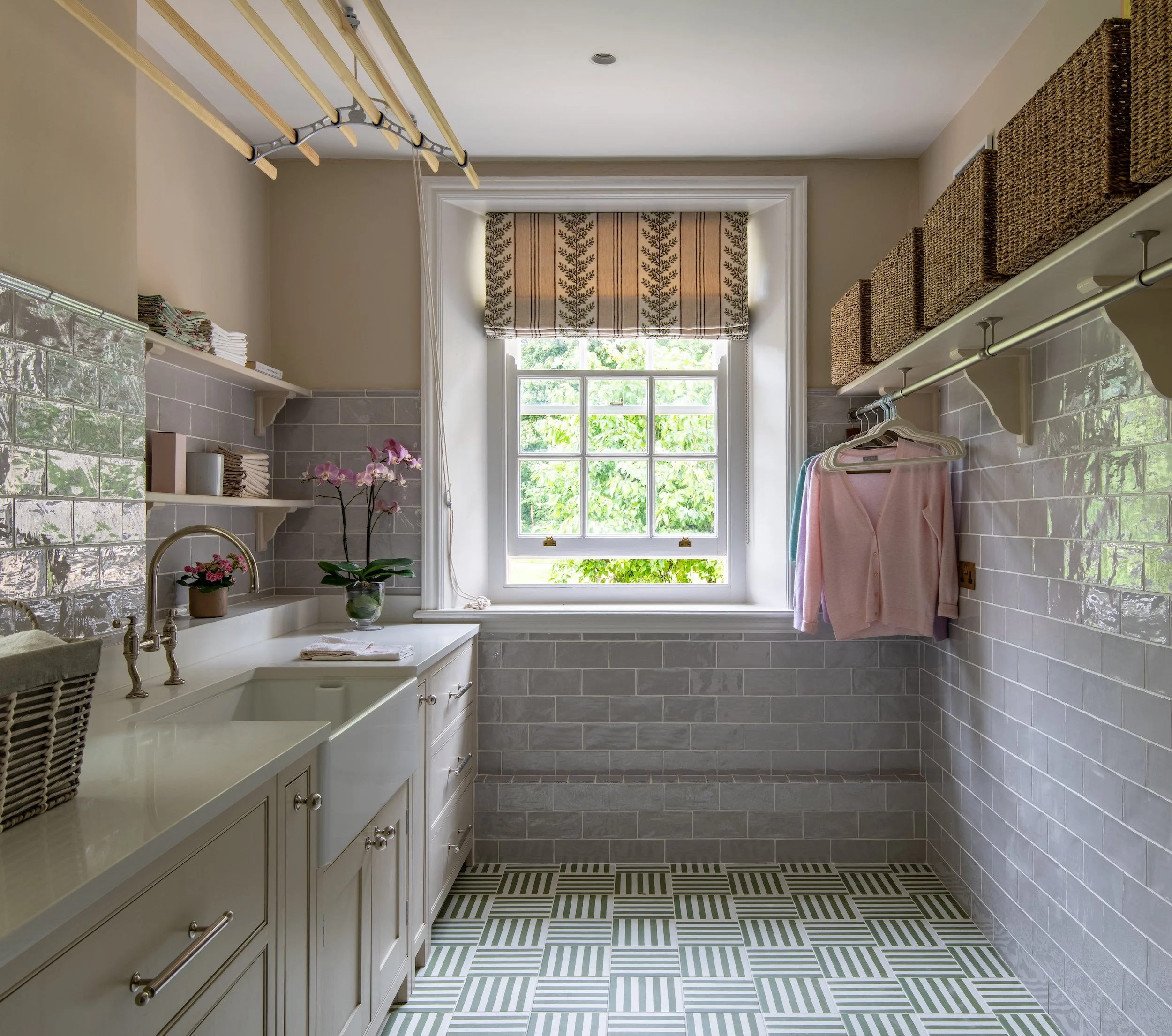 First-floor laundry room designed by MIDA Interiors for a large Cotswolds country estate, transformed from a former guest bedroom with bespoke cabinetry, integrated laundry baskets, dedicated ironing and drying areas, a large handwashing sink and pat
