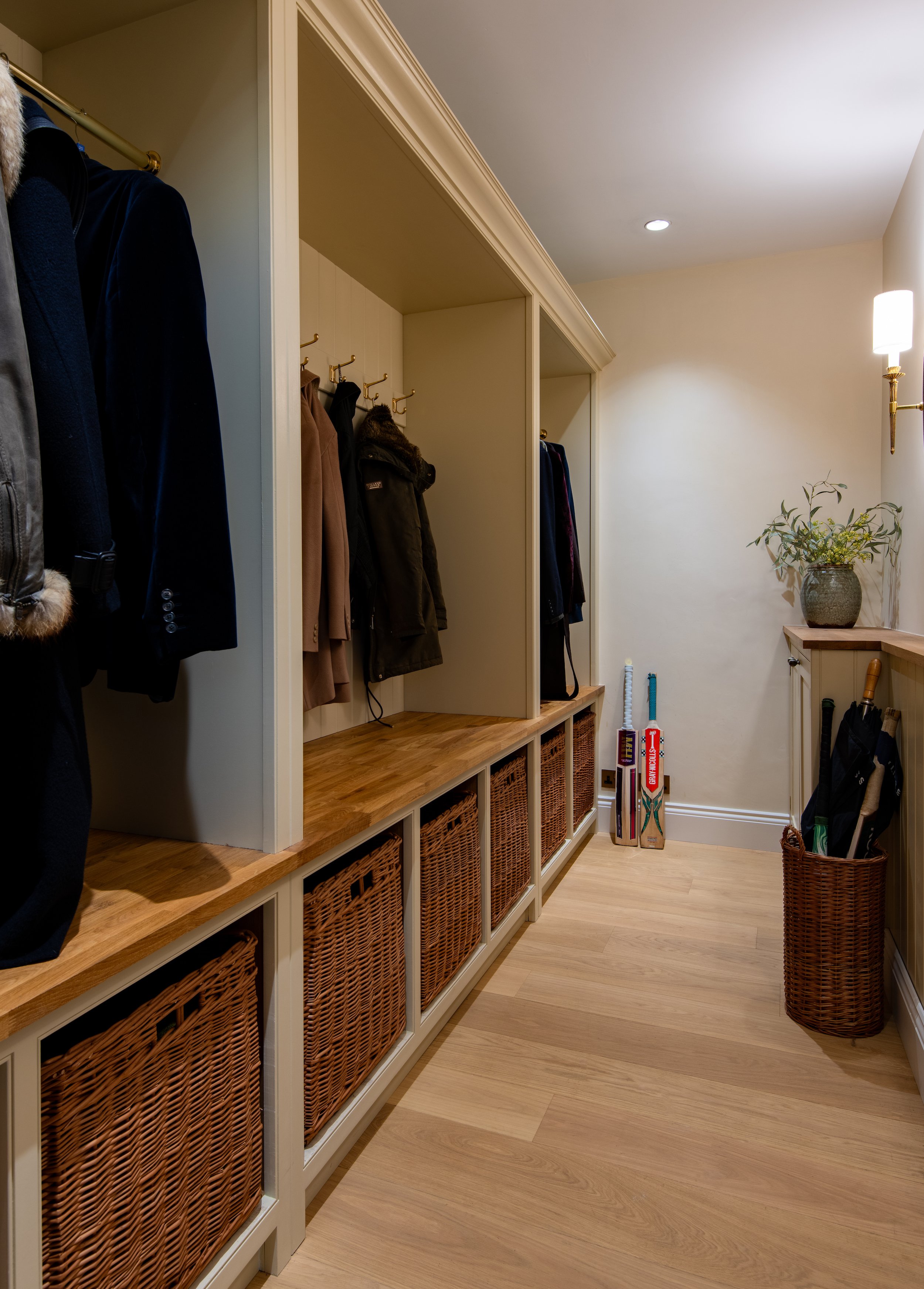 Coat room designed by MIDA Interiors for a large Cotswolds country estate, featuring bespoke open joinery, integrated oak bench seating, wicker basket storage and dedicated space for coats, boots and country pursuits.
