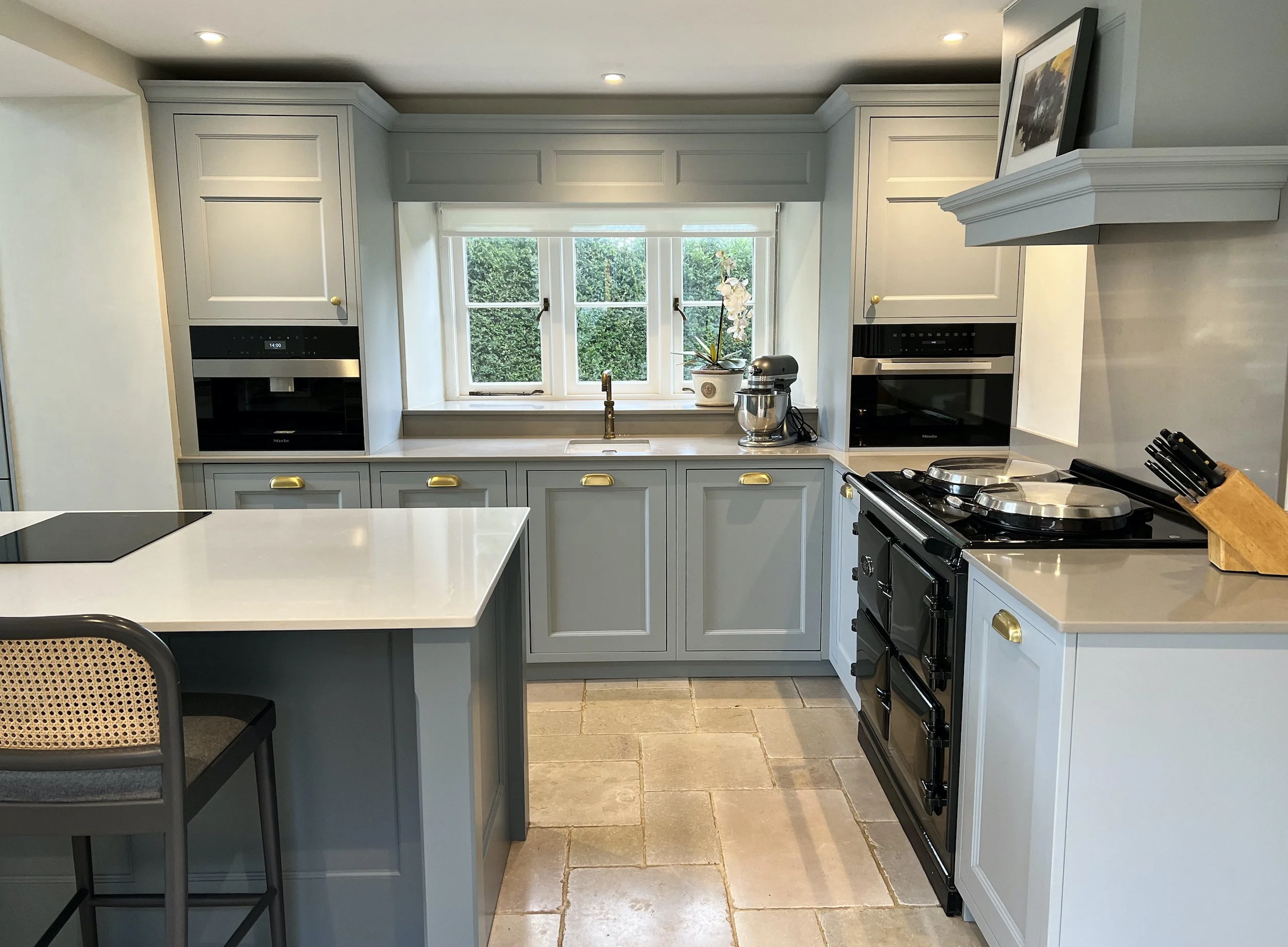 Oxfordshire cottage kitchen featuring tailored grey cabinetry, brass hardware, a generous central island, integrated appliances and a traditional black range cooker.