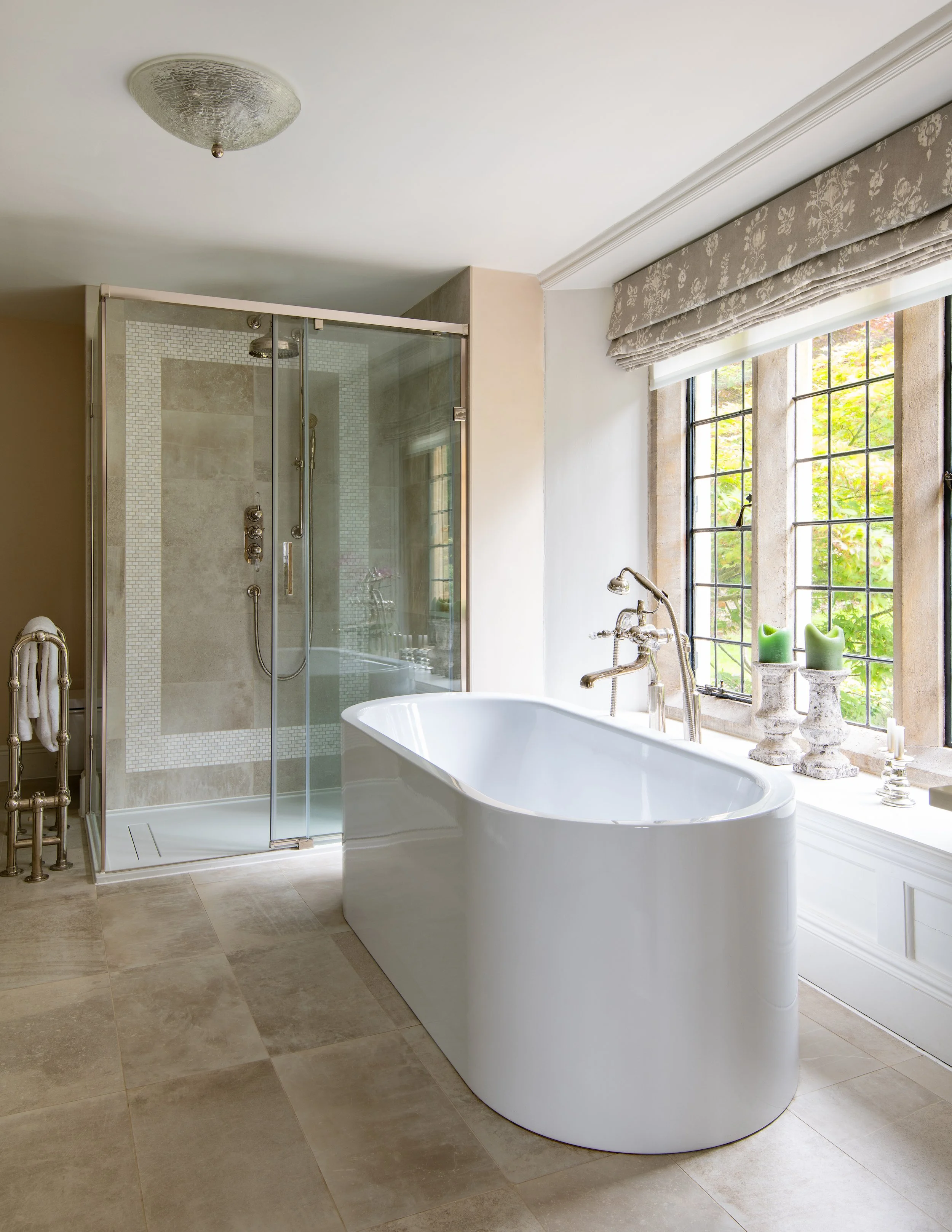 Children’s en-suite bathroom designed by MIDA Interiors for a large Cotswolds country estate, featuring a freestanding bath, substantial walk-in shower, bespoke fittings and tailored Roman blinds beside the original leaded windows.