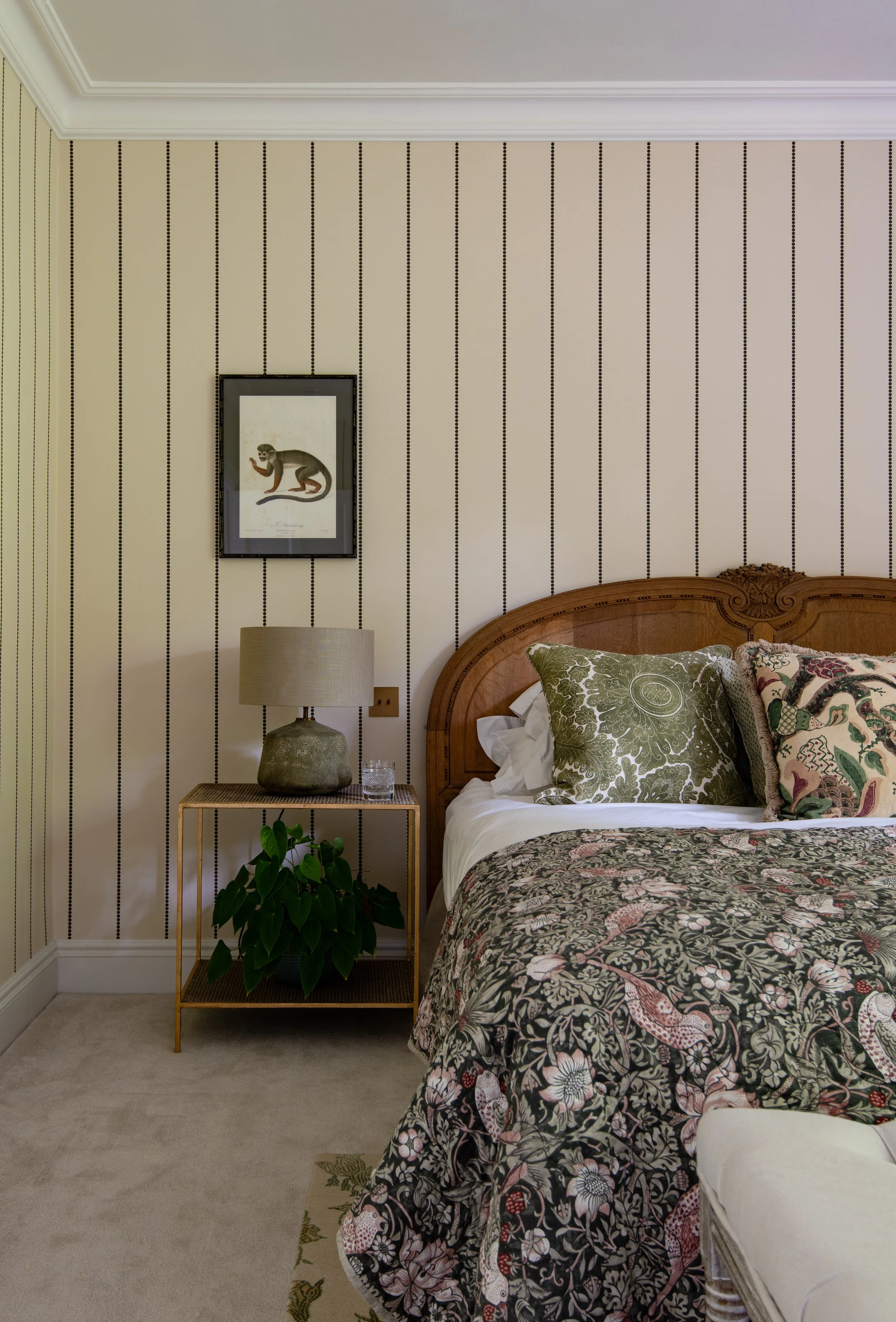Guest bedroom designed by MIDA Interiors for a large Cotswolds country estate, featuring an antique timber bed, richly patterned bedding, striped wallcovering, curated artwork and layered contemporary lighting.
