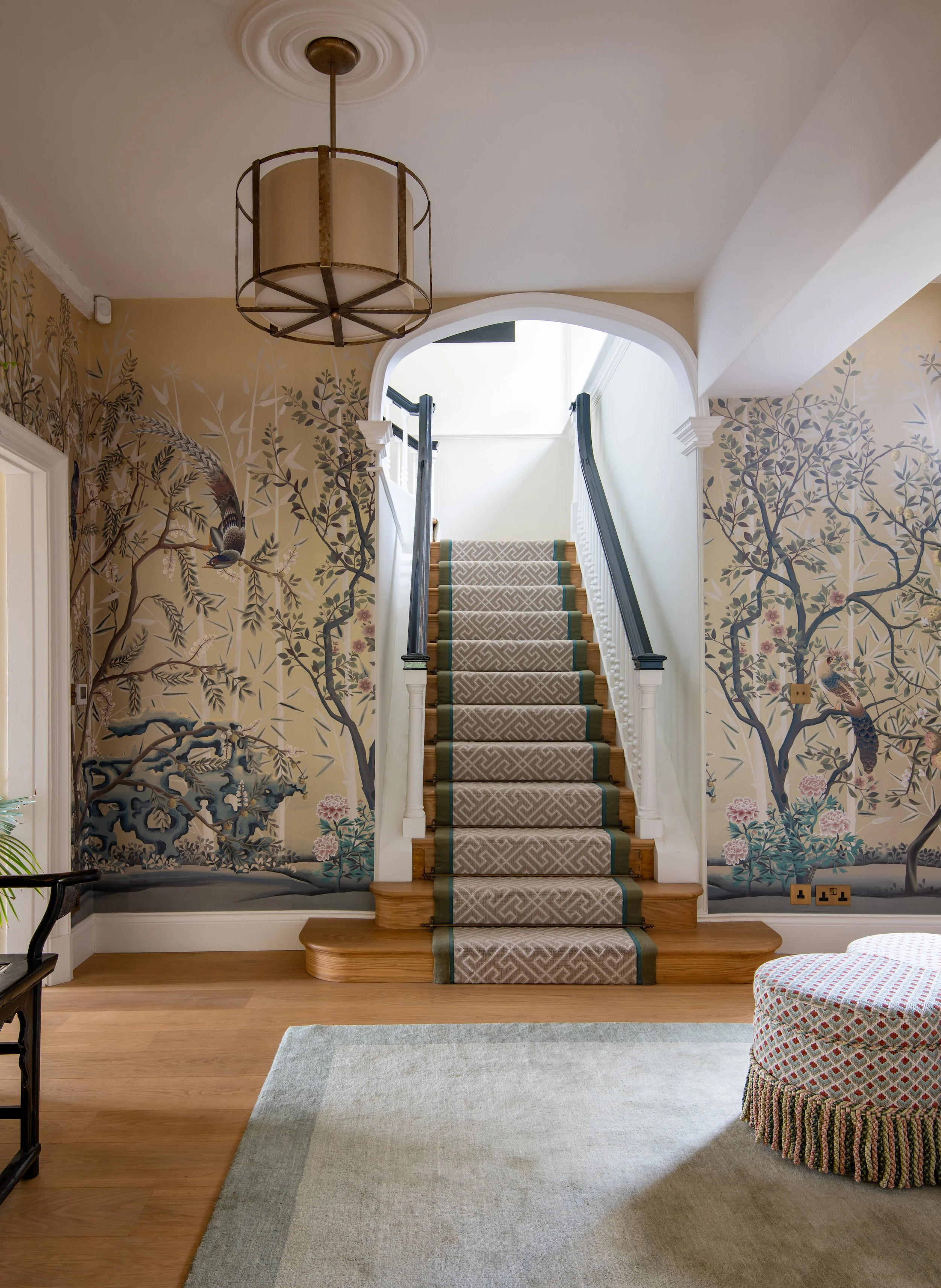 Music hall staircase designed by MIDA Interiors for a large Cotswolds country estate, featuring botanical mural wallpaper, oak flooring, a double-bound patterned stair runner and contemporary statement lighting.
