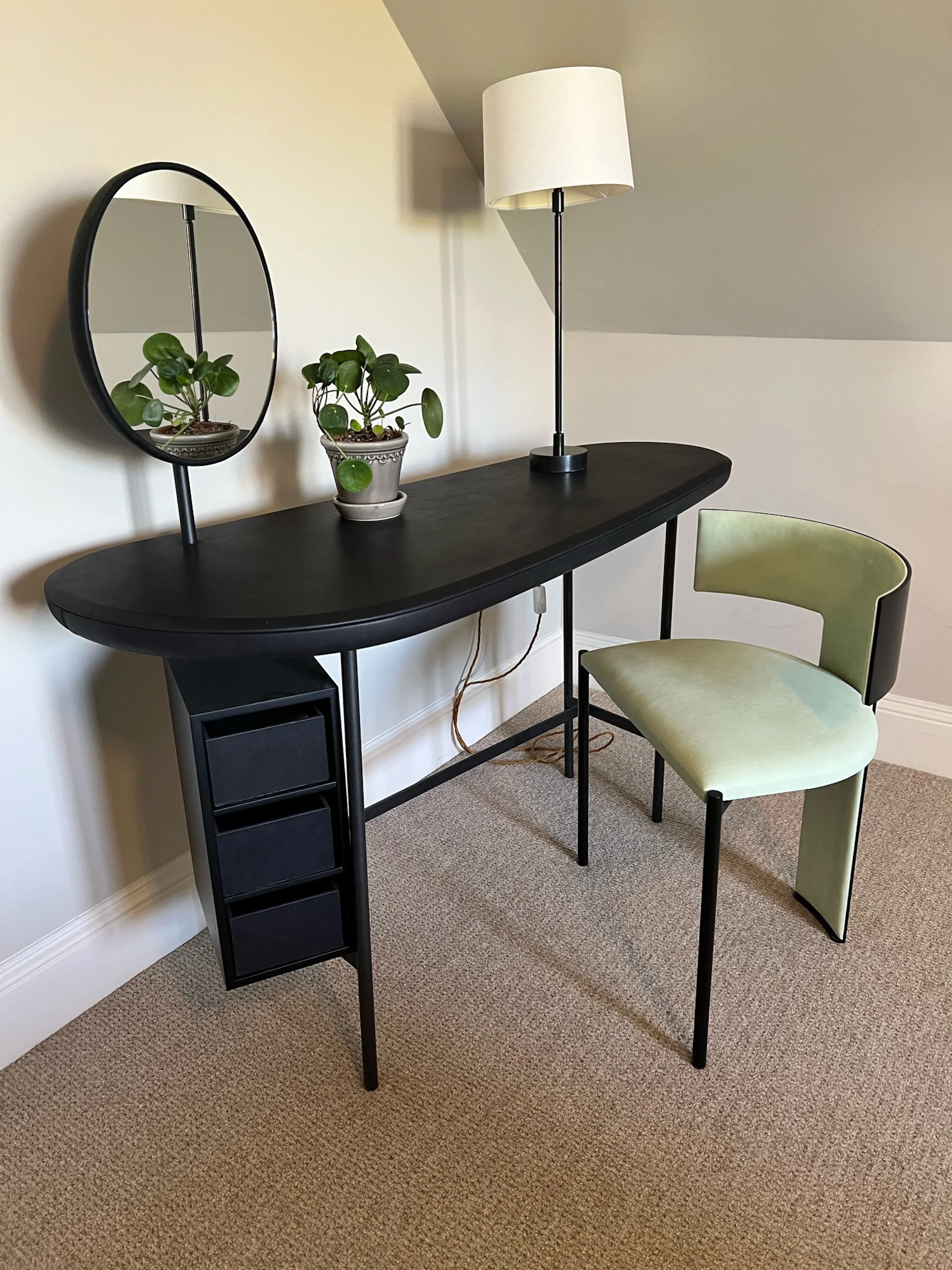 A compact dressing and writing area makes considered use of the guest bedroom’s restricted proportions. The dark, clean-lined table incorporates discreet storage and is paired with an oval mirror, slender reading lamp and tailored chair in a soft gre