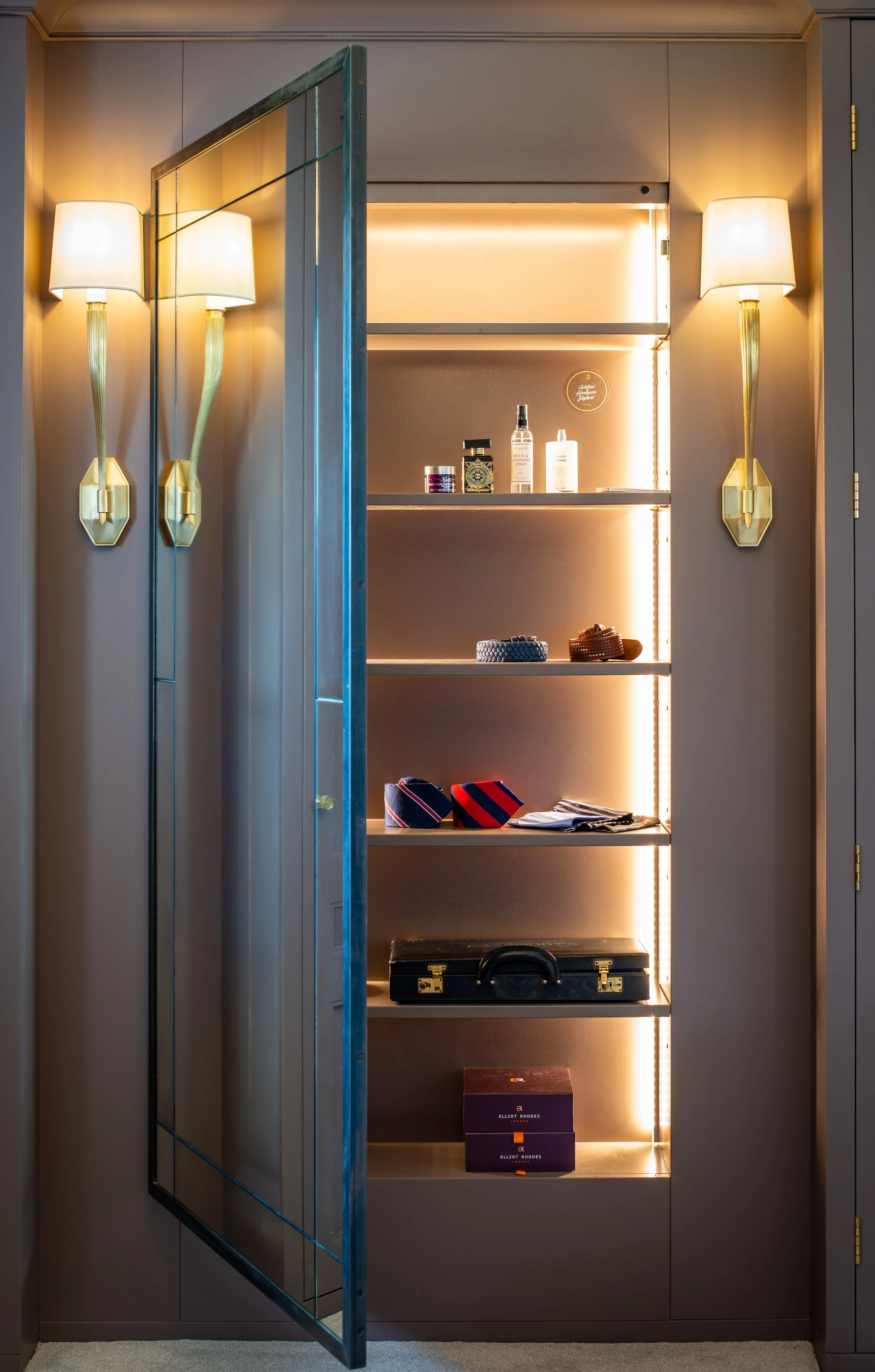 A full-length mirror opens to reveal illuminated accessory storage concealed within the bespoke dressing-room joinery. Carefully spaced shelves organise ties, belts, grooming products and personal objects, demonstrating how practical storage was inte
