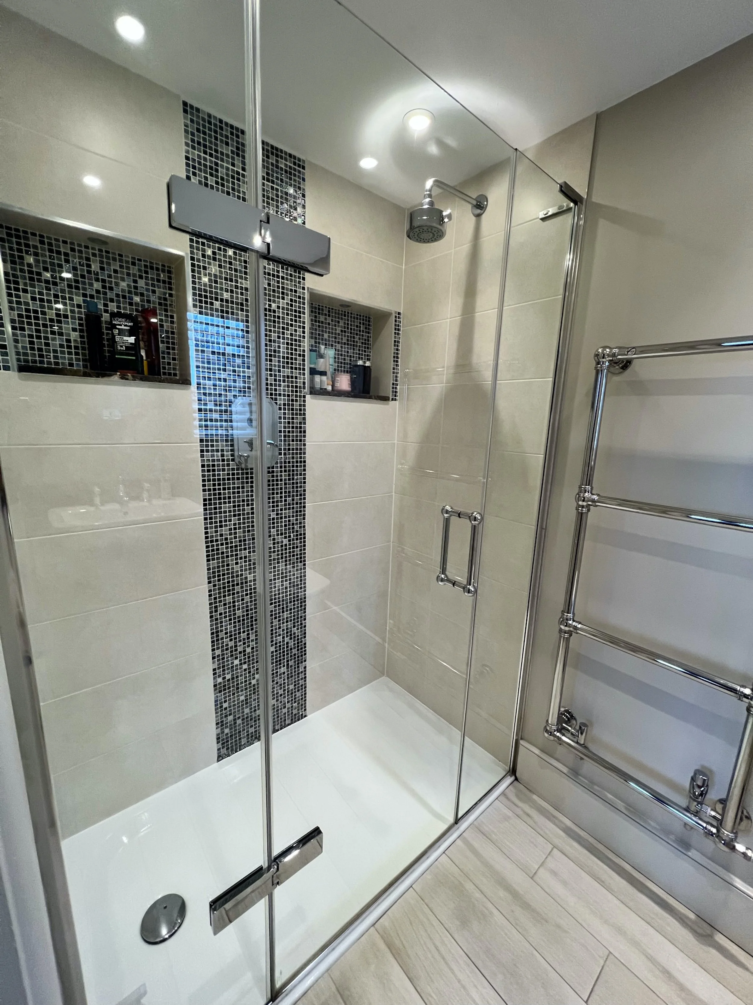 Principal en suite with a frameless walk-in shower, recessed storage niches, monochrome mosaic detailing and a polished chrome heated towel rail.