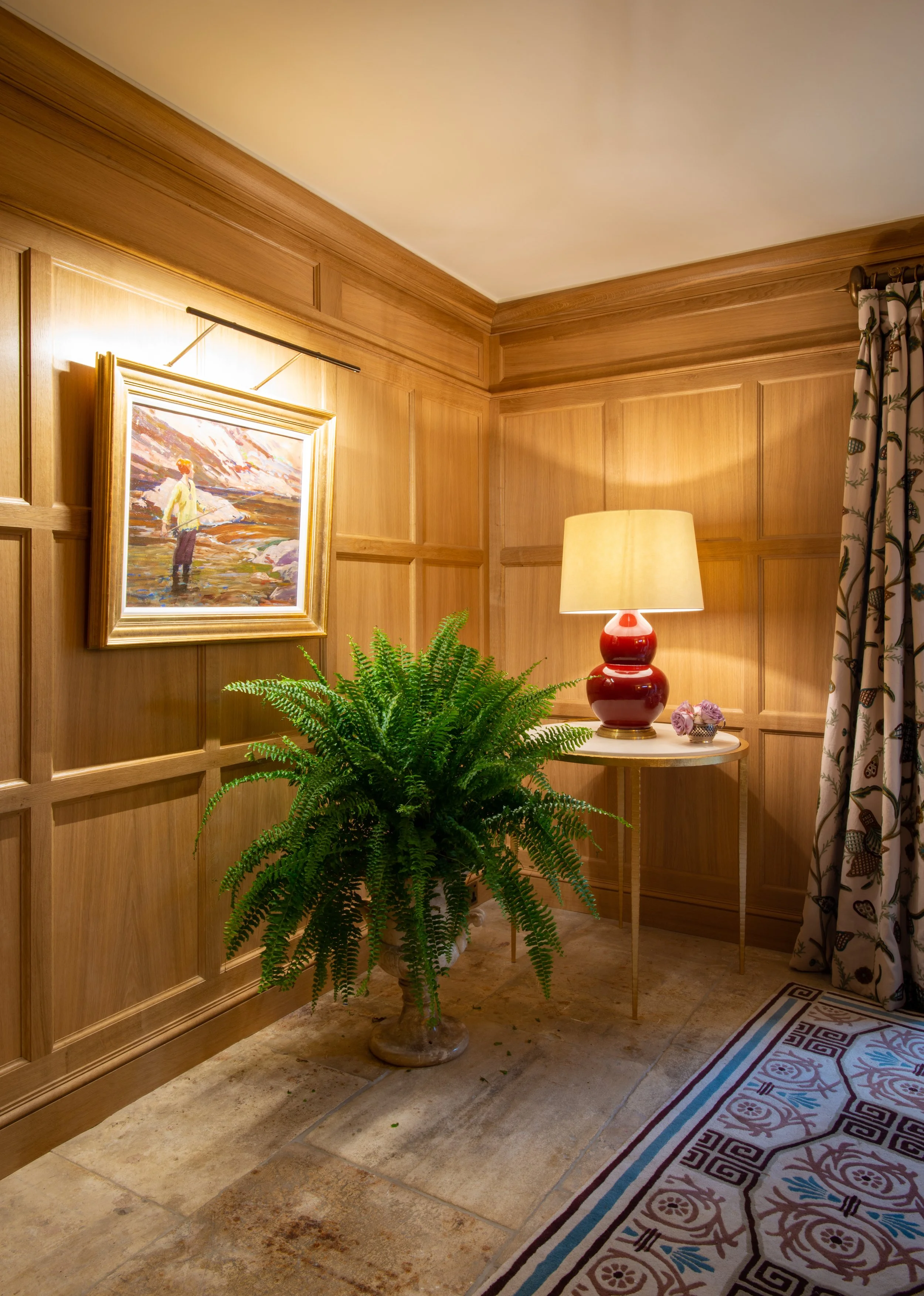A detailed view of the handcrafted oak panelling designed and installed around the dining room’s distinctive proportions. The warm timber is balanced by contemporary artwork, a sculptural red table lamp and patterned crewelwork curtains. The original