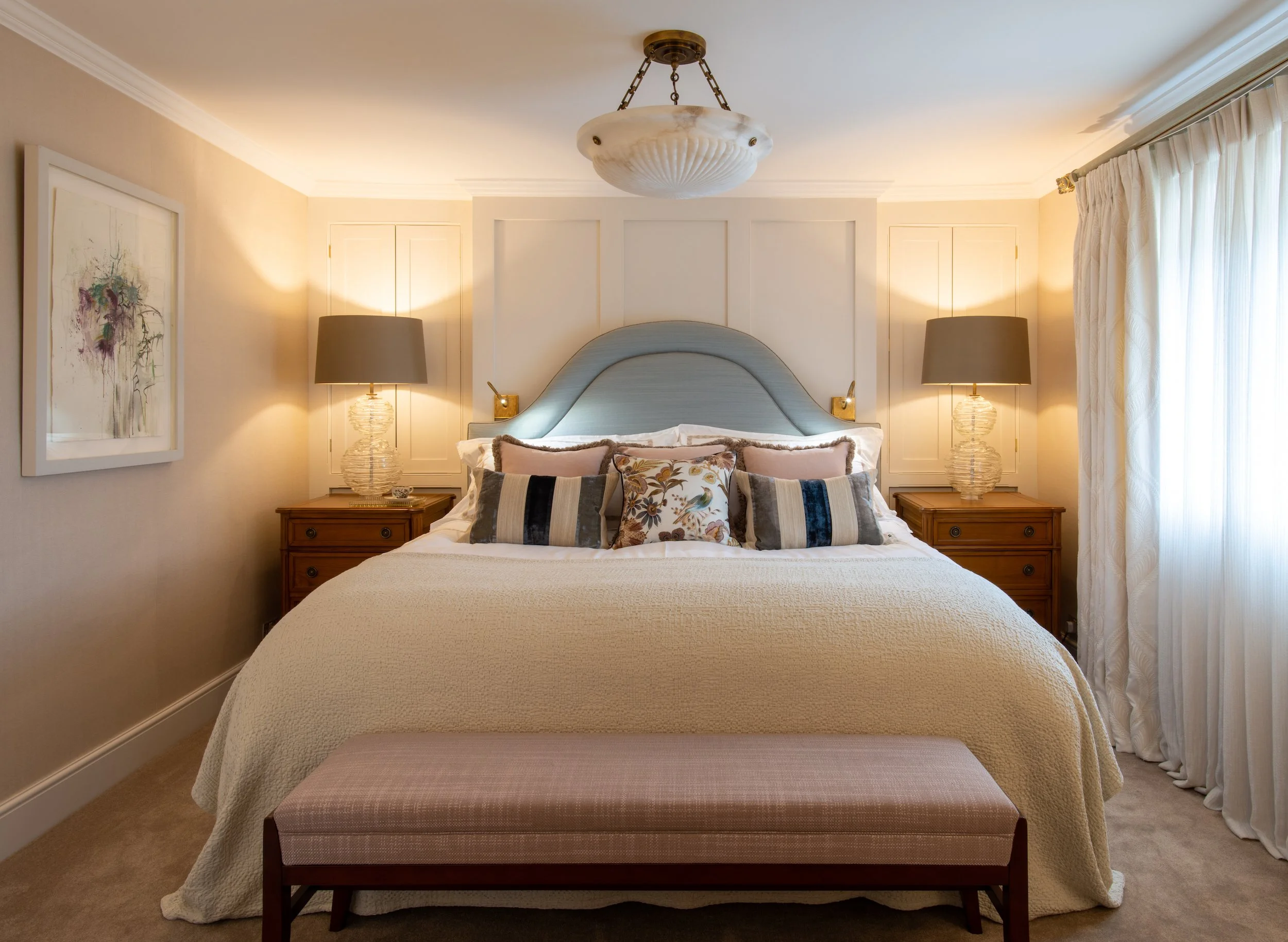 Luxury principal bedroom designed by MIDA Interiors for a Cotswolds country house and estate, featuring a bespoke upholstered headboard and mattress, integrated joinery, layered textiles and elegant decorative lighting.