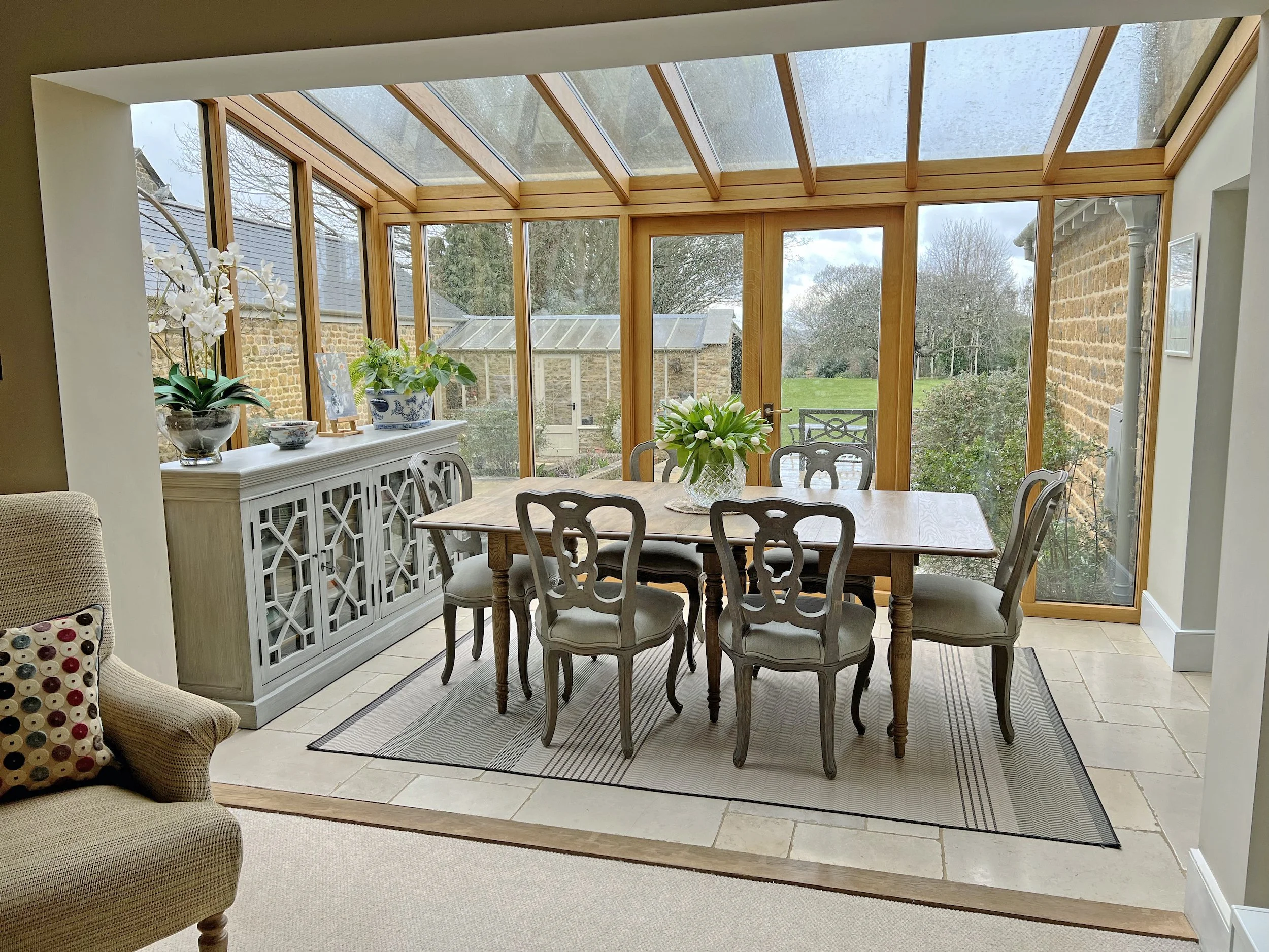 Light filled dining room in a timber framed garden room adjoining a 19th-century Oxfordshire cottage, with exposed stonework and views across the garden.