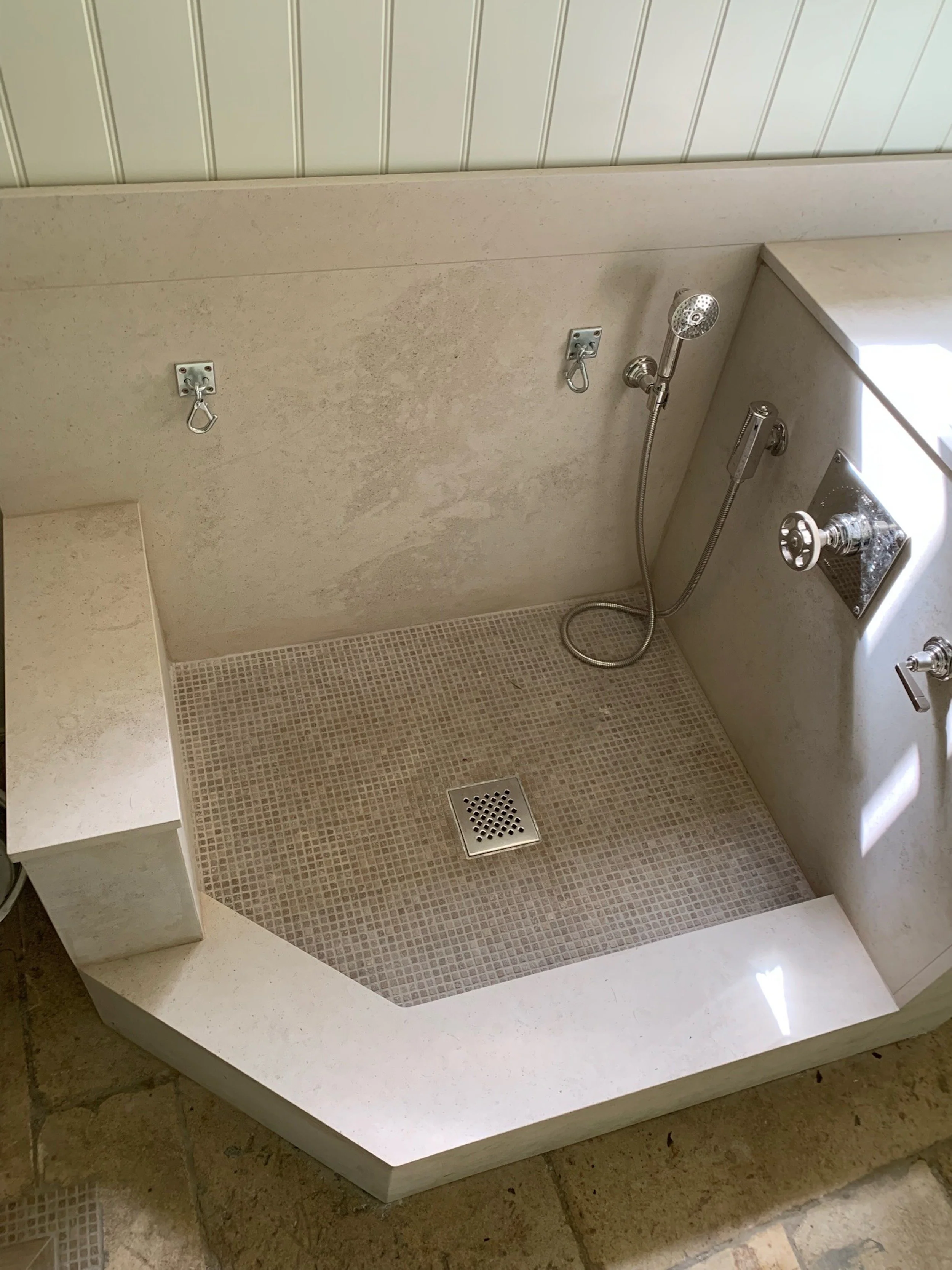 A purpose-designed dog shower within the Cotswold farmhouse utility room, featuring a low-threshold mosaic wet floor with central drainage, a handheld shower, chrome controls and wall-mounted restraint points. The generous opening accommodates dogs o