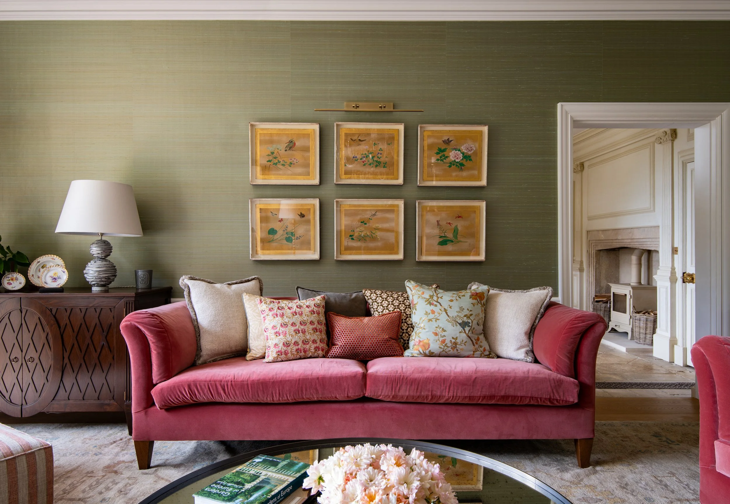 Drawing room designed by MIDA Interiors for a large Cotswolds country estate, featuring a bespoke sumptuous pink velvet sofa, curated artwork, silk walling, layered cushions and antique furniture arranged for elegant family living.