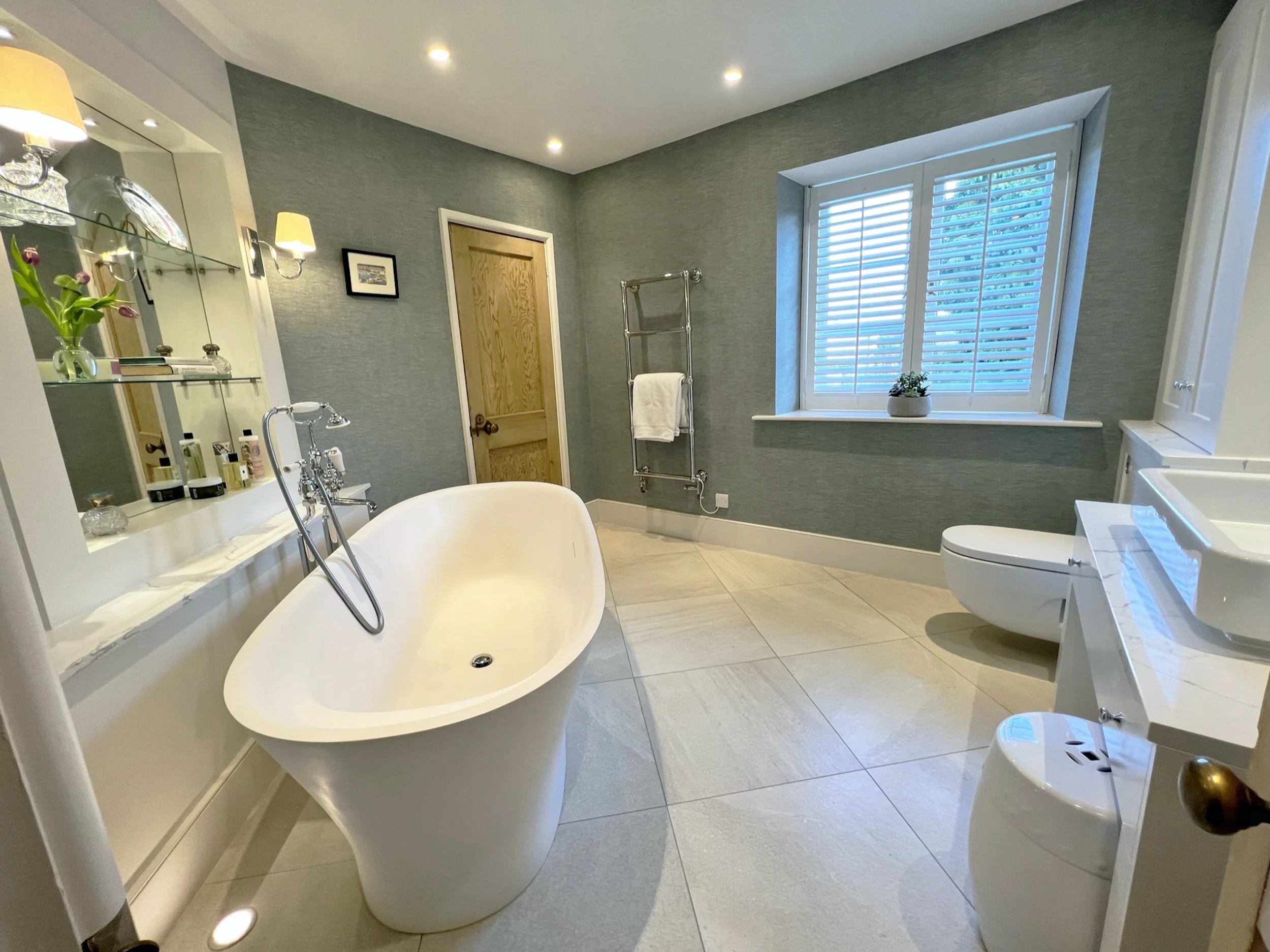 Jack and Jill family bathroom in a 19th-century Oxfordshire cottage, featuring a freestanding bath, tailored joinery, linen look wallpaper and a new tiled floor.