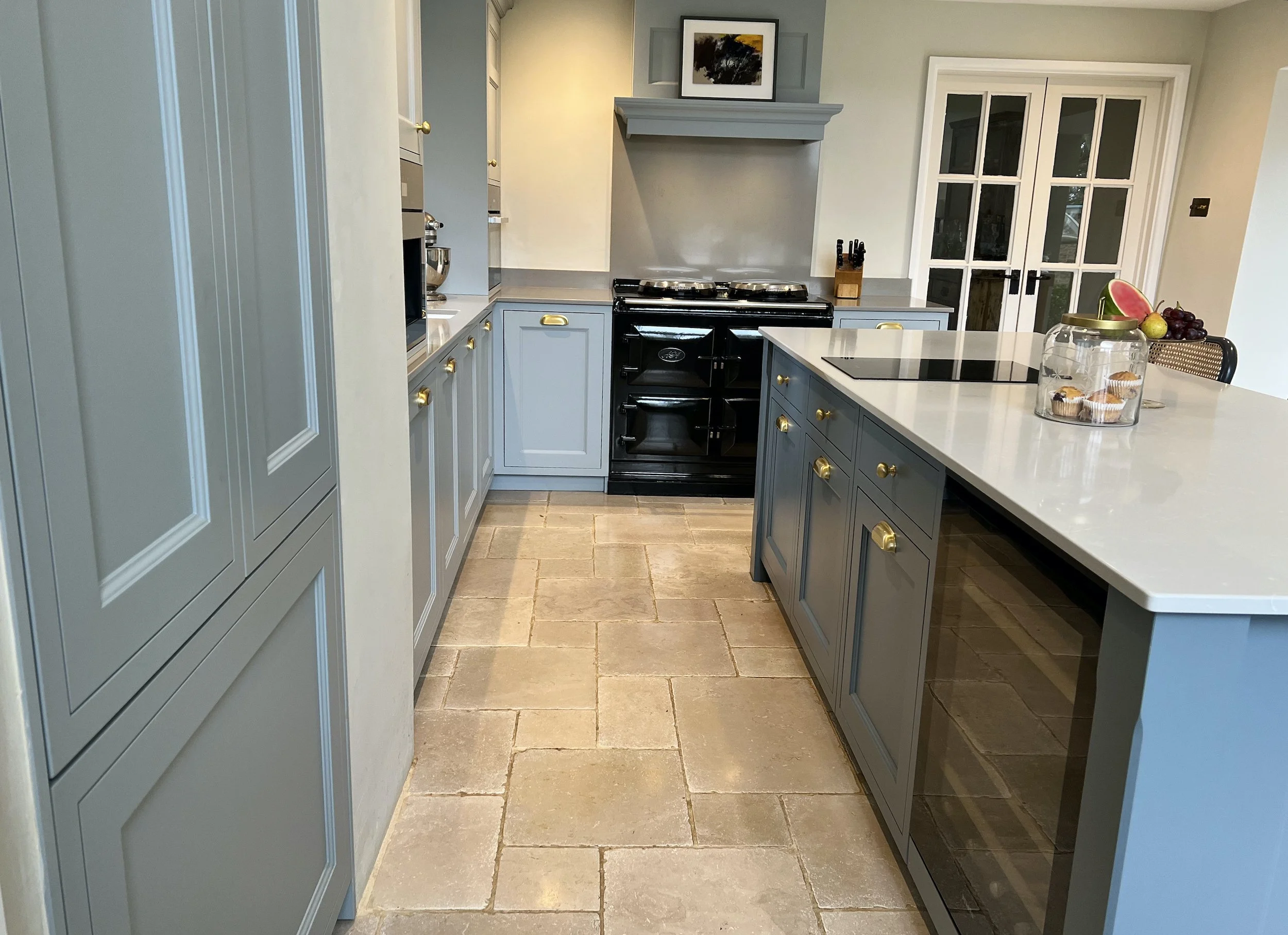 Traditional country kitchen with a black range cooker, painted Shaker cabinetry, brass handles, pale stone worktops and a practical central island.
