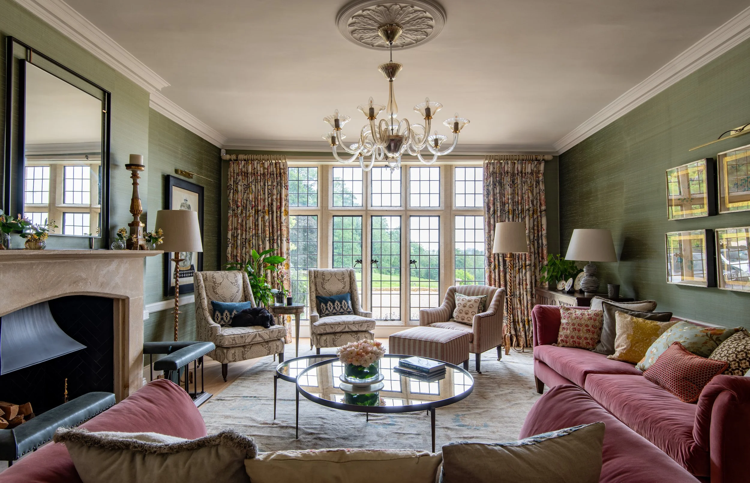 Grand drawing room designed by MIDA Interiors for a large Cotswolds country estate, featuring silk walling, bespoke furniture, antique rugs used to define seating areas, a retained stone fireplace and a Murano glass chandelier.