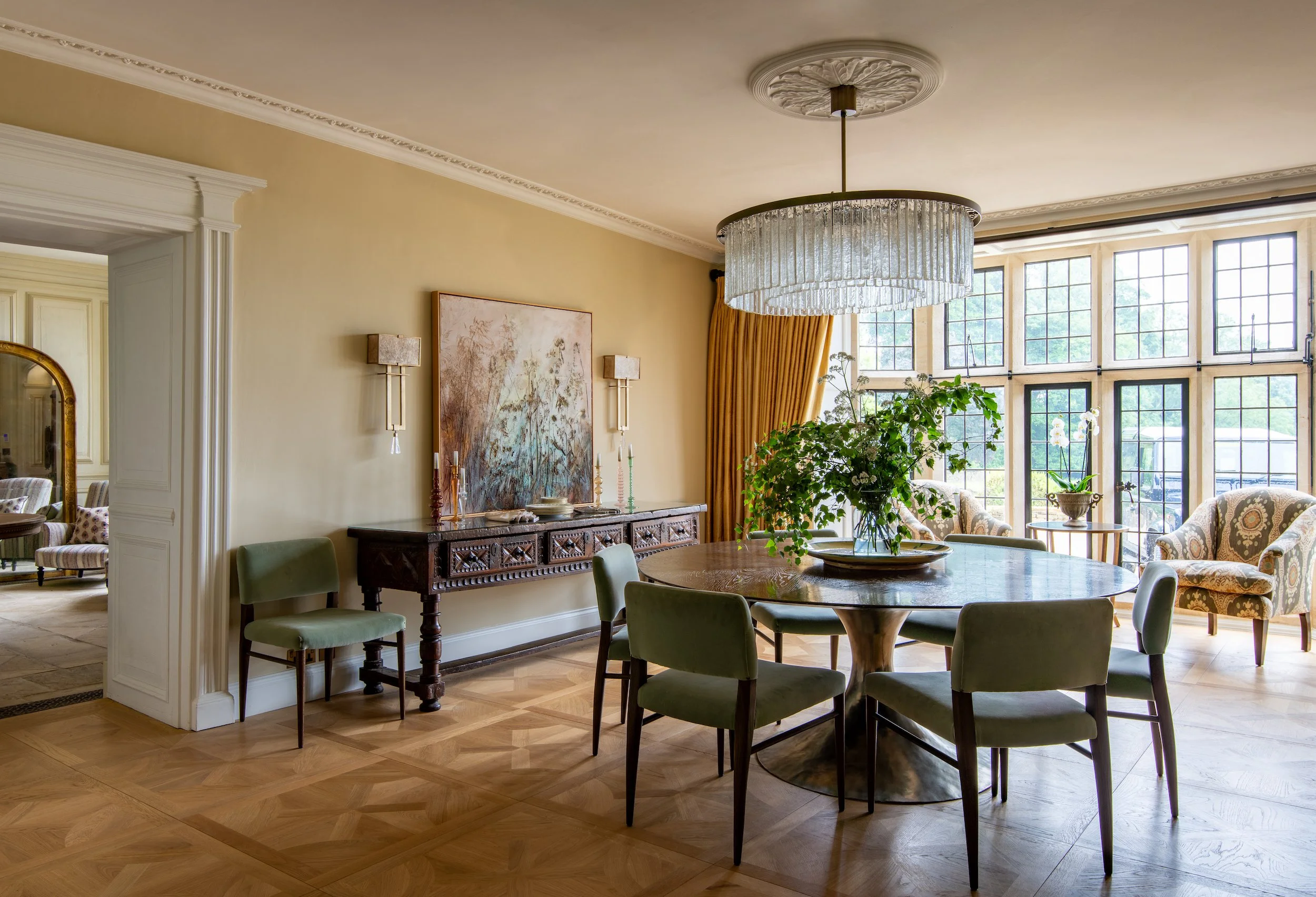 Luxury dining room designed by MIDA Interiors for a large Cotswolds country estate, featuring bespoke furniture, parquet flooring, period detailing, a statement chandelier and garden views.