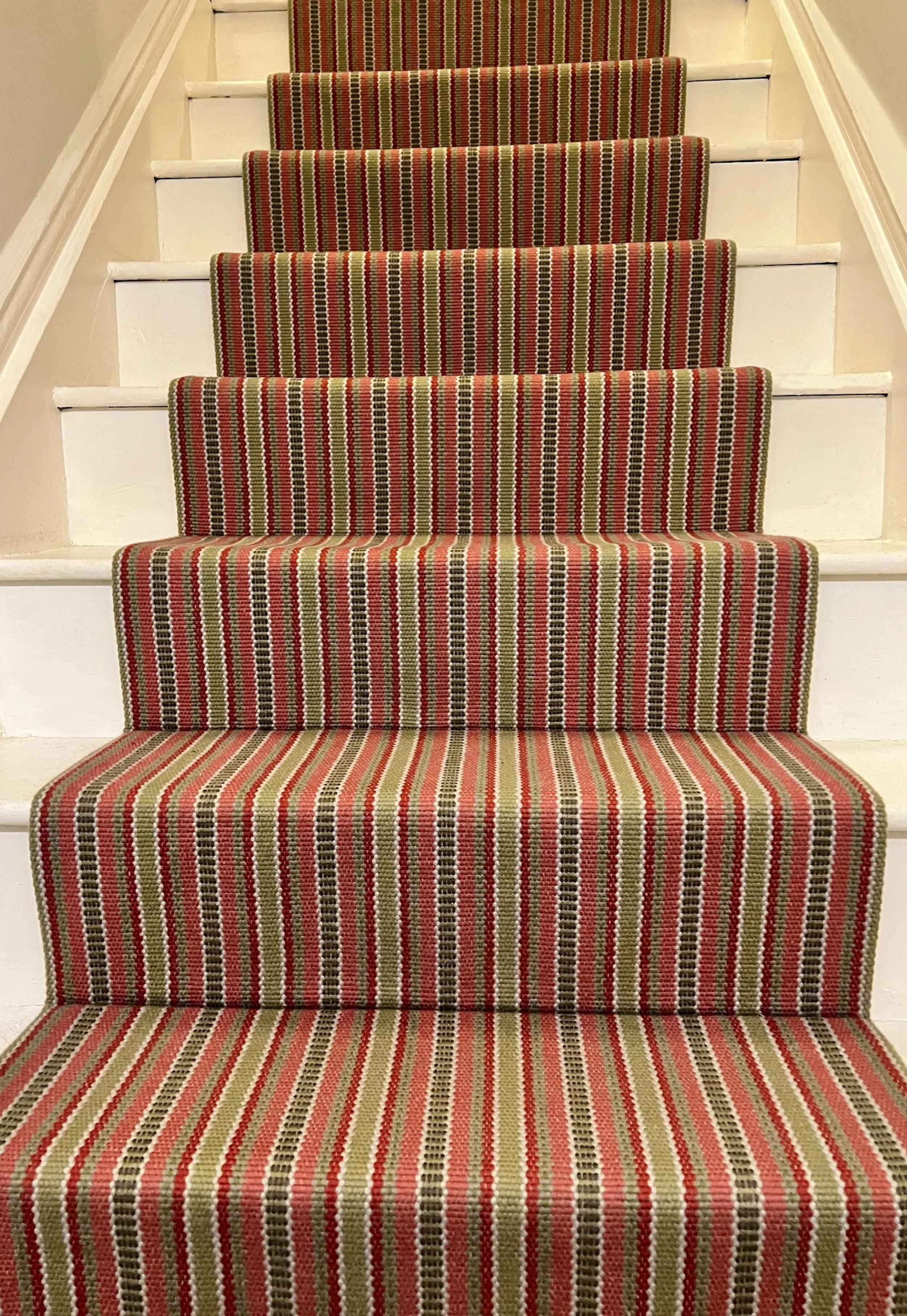 Painted timber staircase in a 19th-century Oxfordshire cottage, finished with a cheerful striped stair runner in red, olive and neutral tones.