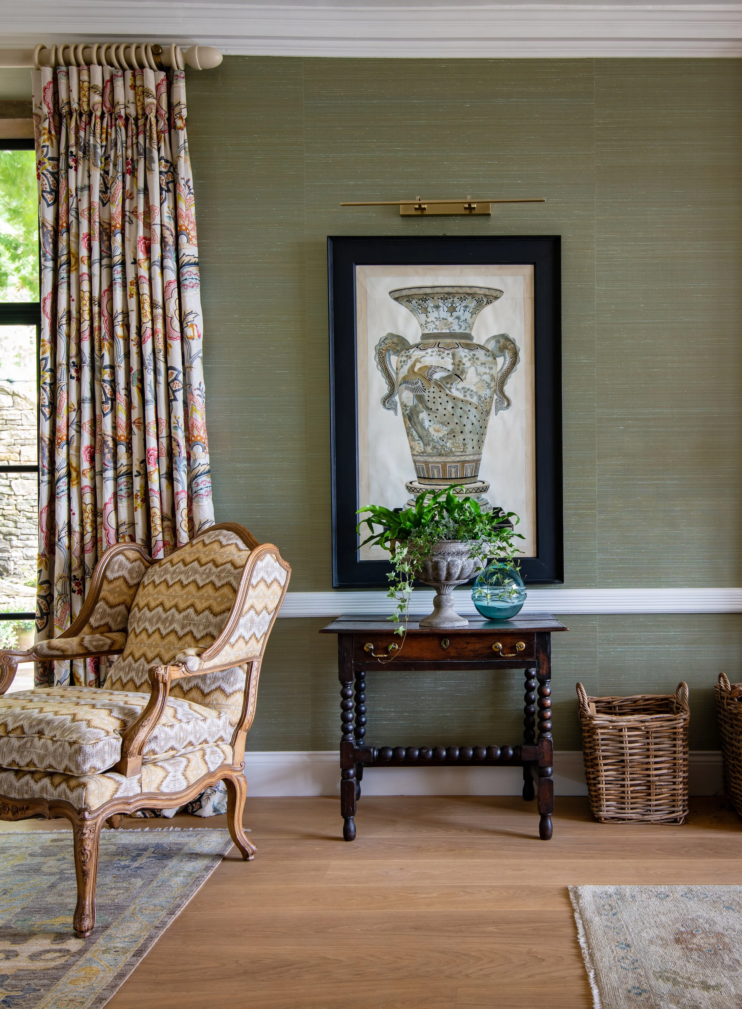 Drawing room detail designed by MIDA Interiors for a large Cotswolds country estate, featuring a sourced antique French armchair reupholstered for the scheme, curated artwork, silk walling, picture lighting and an antique side table.