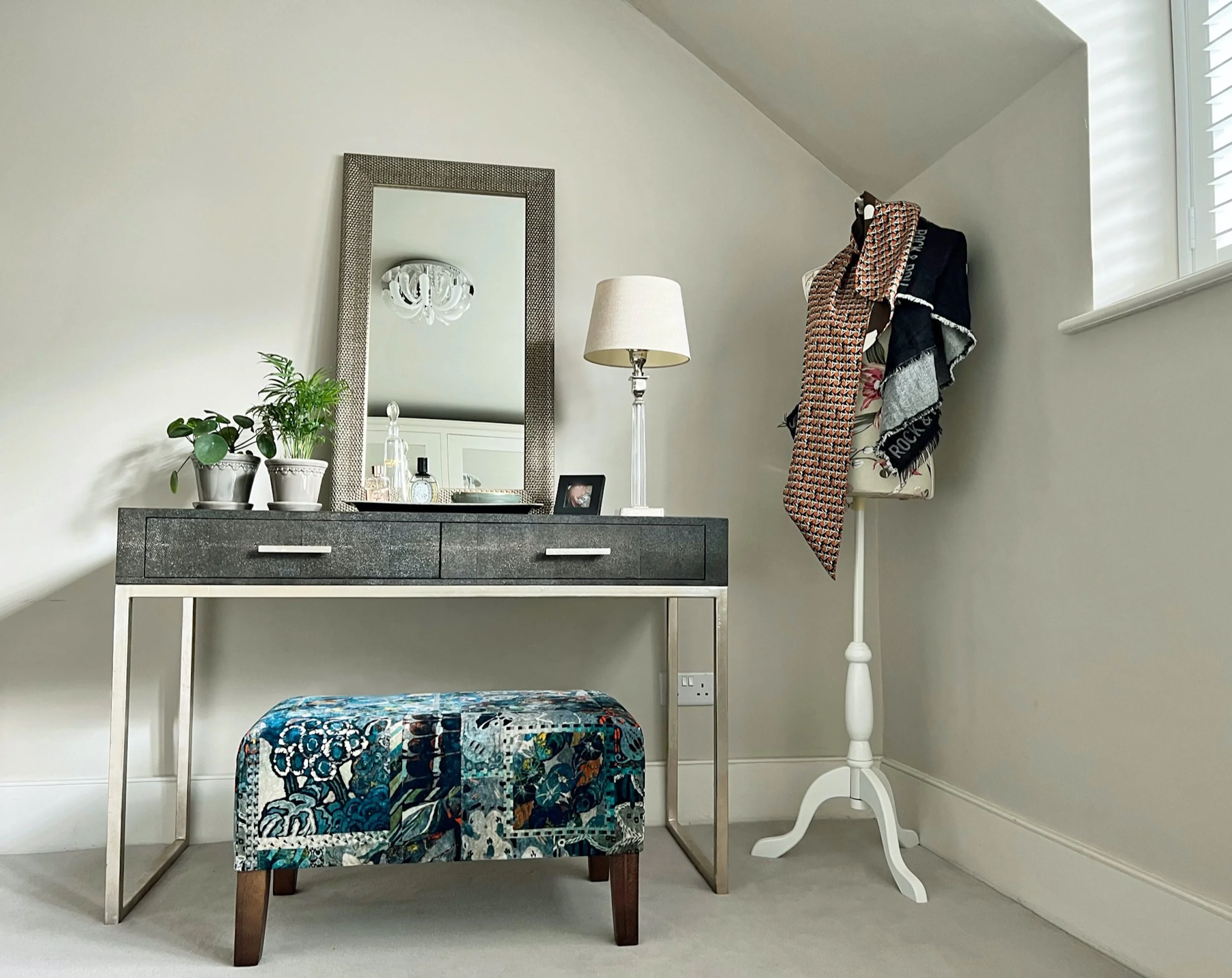 Refined dressing area featuring a slimline dressing table, textured mirror, patterned upholstered stool and carefully considered decorative lighting.