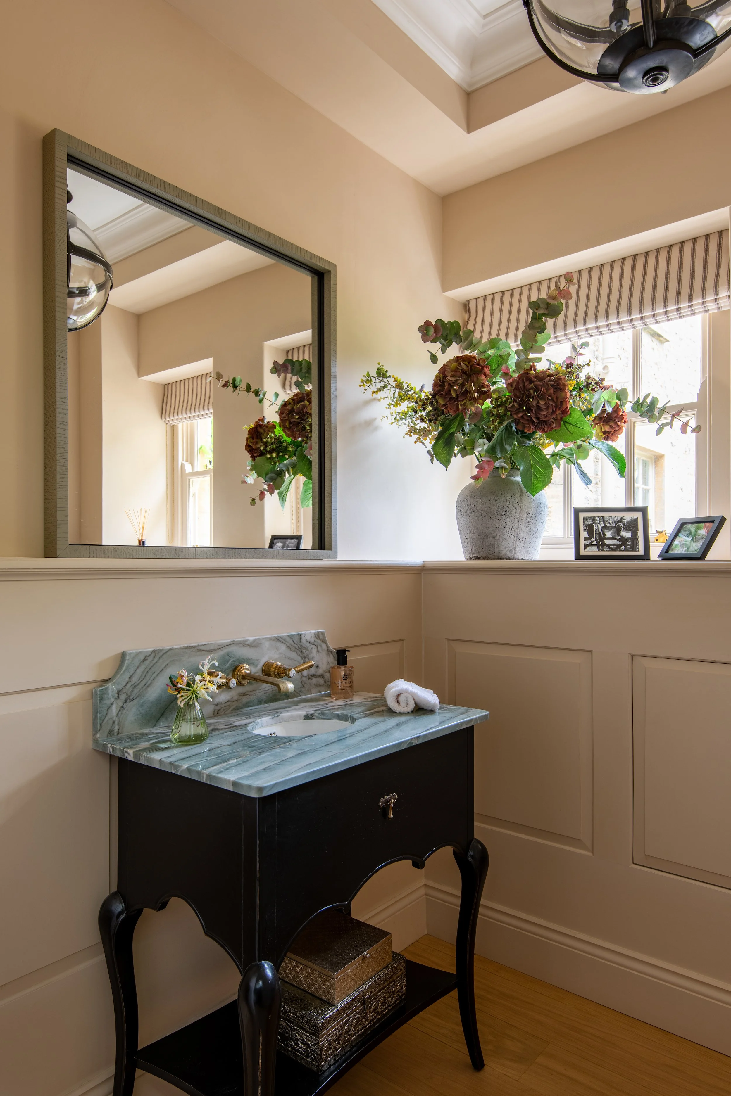 Powder room designed by MIDA Interiors for a large Cotswolds country estate, featuring a reconfigured layout, bespoke vanity with natural stone top, panelled walls and concealed storage.