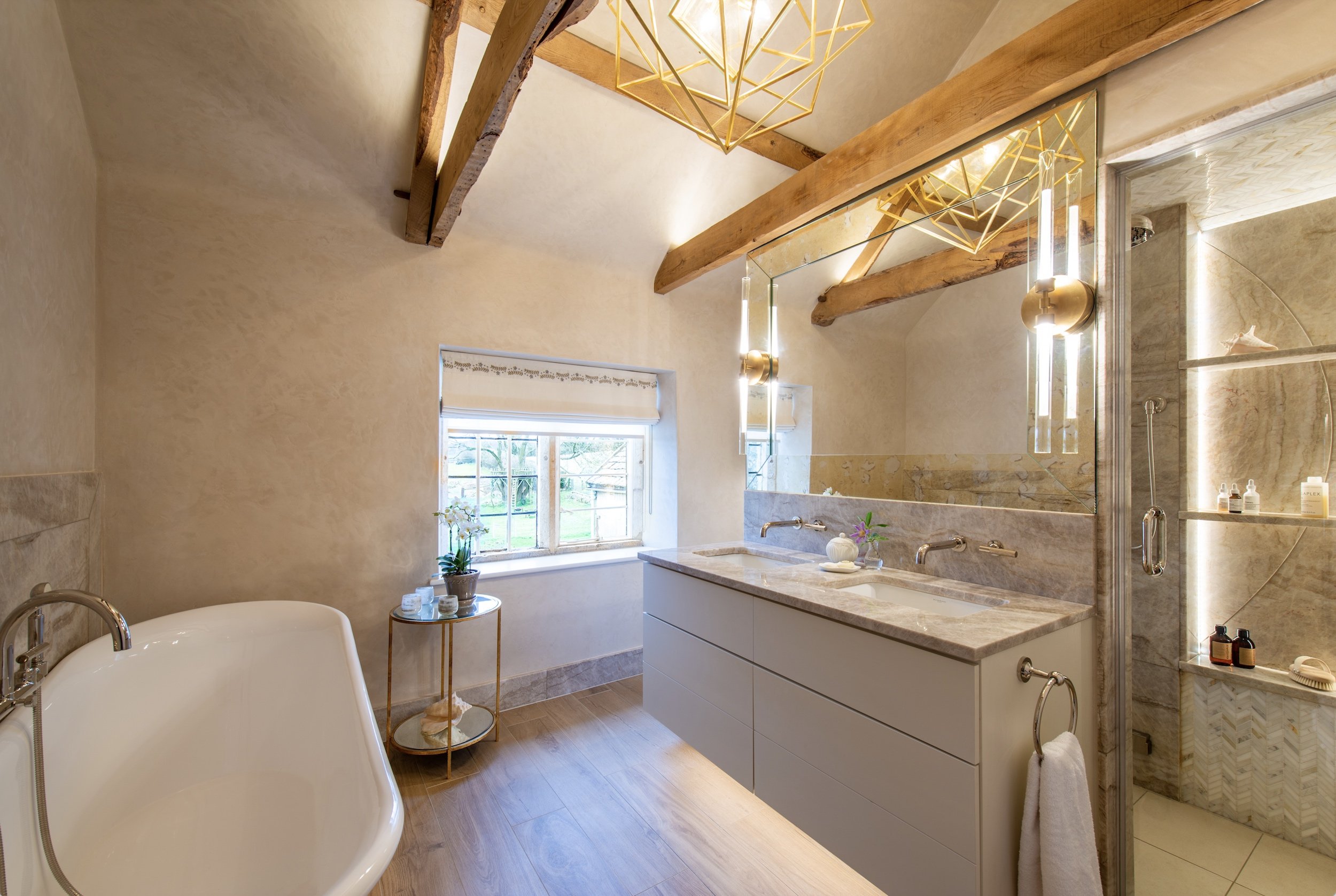 Luxury bathroom designed by MIDA Interiors for a Cotswolds country house, featuring Venetian plaster walls, exposed oak beams, a brass roll-top bath and a bespoke arched ceiling steam shower.