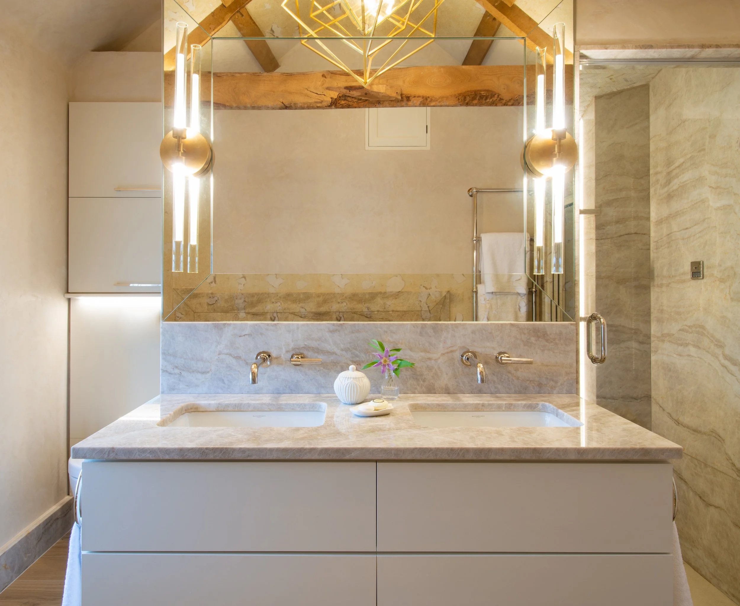 A wall hung double vanity provides individual basins and generous concealed storage within the principal bathroom. The restrained cabinetry is paired with a veined stone worktop and splashback, wall mounted fittings and an expansive mirror. Contempor