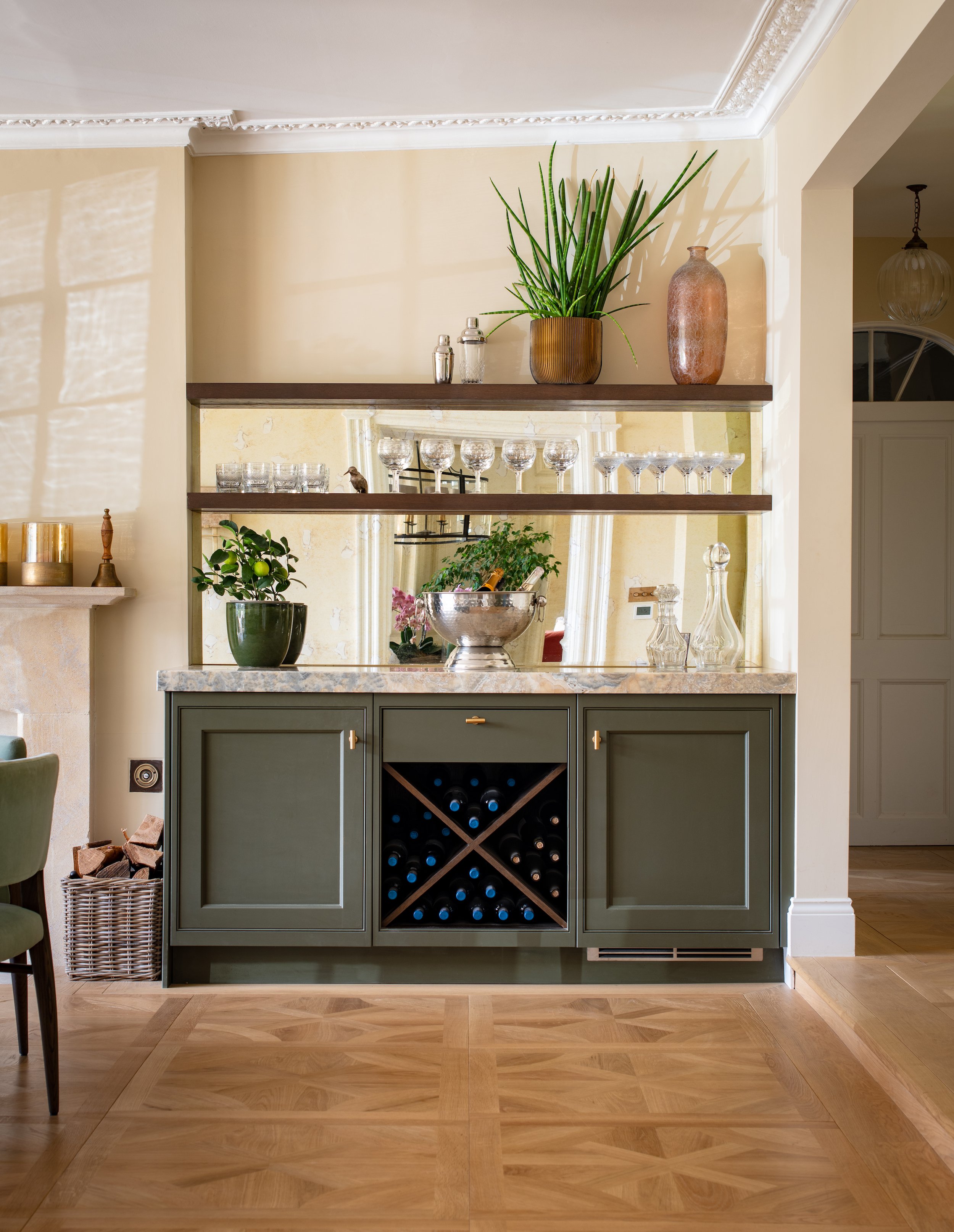 Bespoke dining room bar designed by MIDA Interiors for a large Cotswolds country estate, featuring handcrafted cabinetry, integrated wine storage, illuminated mirrored shelving and an Onice Black Cloud stone worktop.