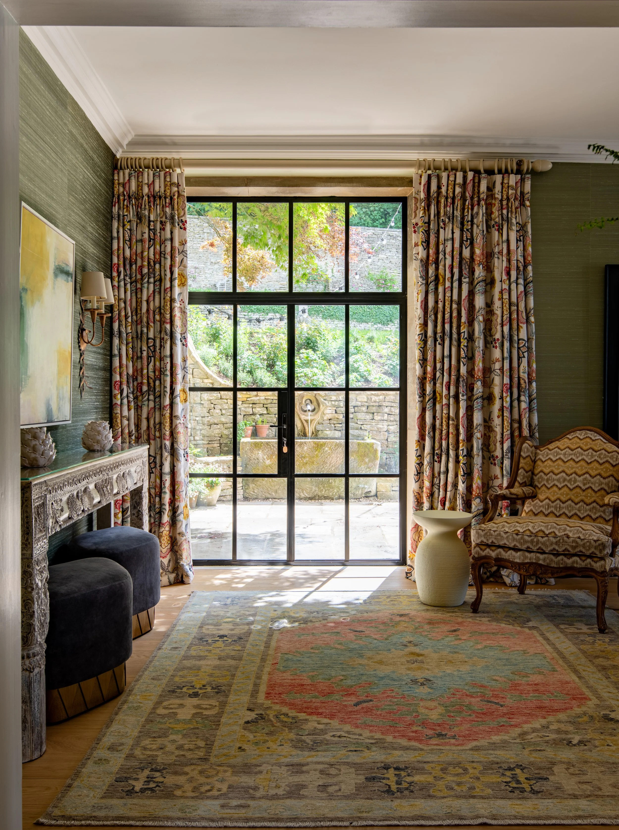 Drawing room designed by MIDA Interiors for a large Cotswolds country estate, featuring silk walling, an antique rug, reupholstered French seating and Crittall French doors opening onto the garden terrace for seamless indoor-outdoor entertaining.