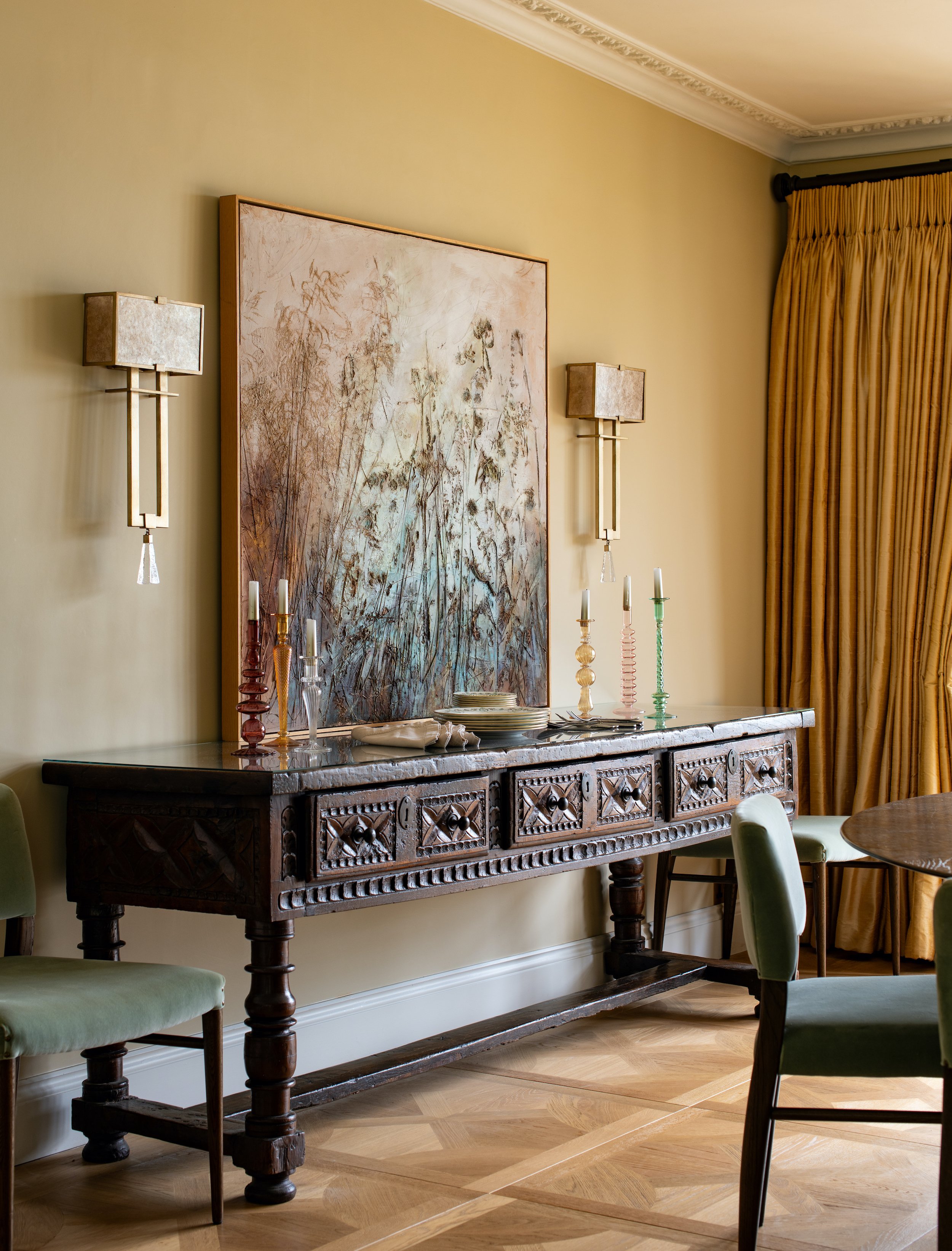 Dining room detail designed by MIDA Interiors for a large Cotswolds country estate, featuring an antique Spanish sideboard, curated contemporary artwork, decorative wall lights and Venetian-style parquet flooring.