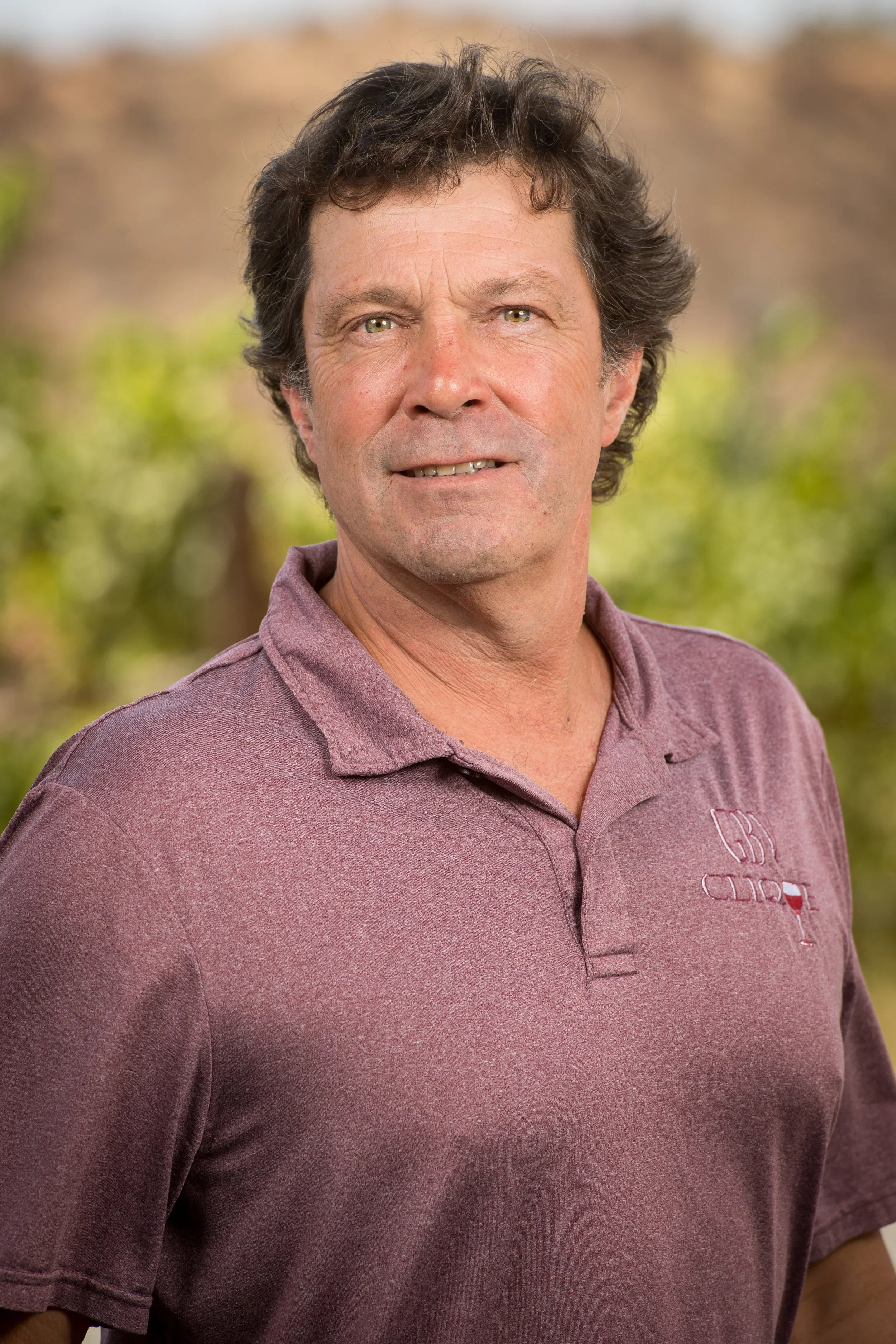Man in a maroon polo shirt posing outdoors with a blurred natural background.