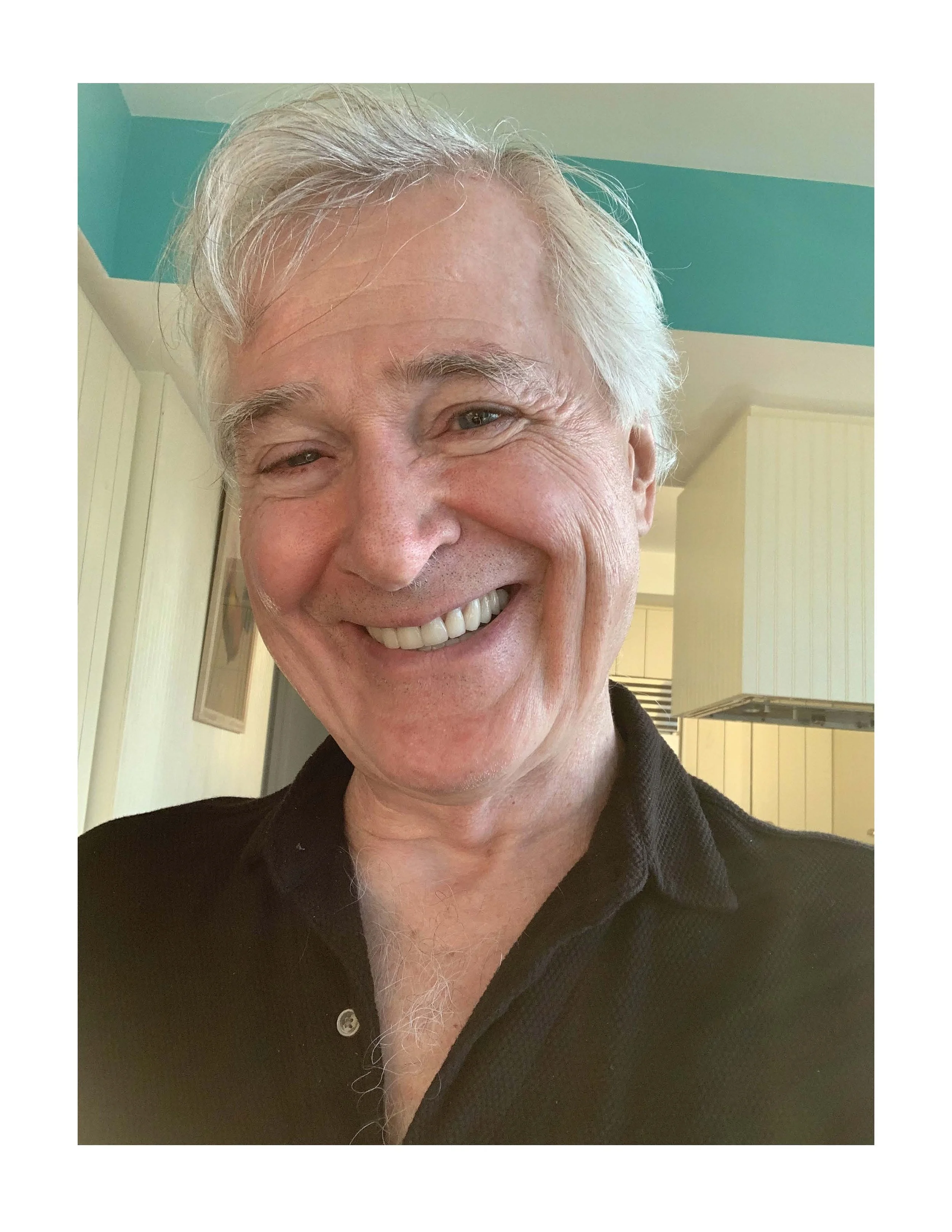 John Patrick Shanley is a light-skinned older man with white hair. He’s wearing an olive shirt and smiling.