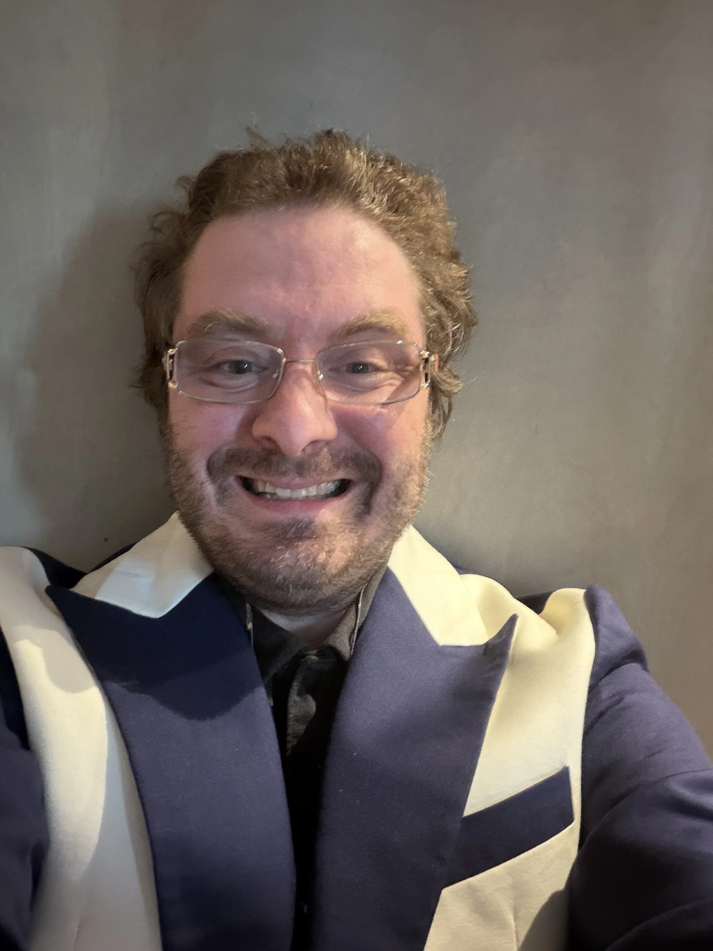 Keith Murfee-DeConcini, Board Member. A man who is in his 30’s, white skin, curly light brown hair and facial hair. He is wearing glasses and a blue and white collared jacket.