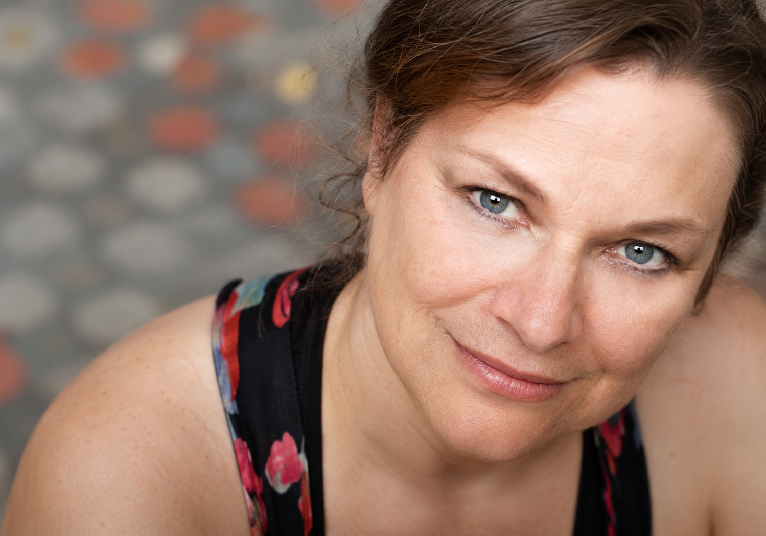 Anita Hollander, Board Member. A light-skinned woman, 60s, blue eyes, brown hair. She wears a sleeveless red and black floral top.
