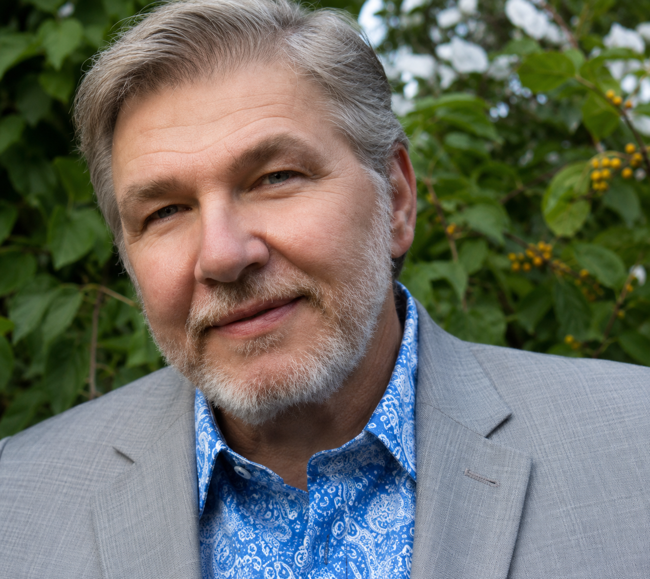 Richard M. Rose (Board Member). Light-skinned man, 60s, gray hair and beard. He wears a gray blazer and a patterned blue-collar shirt.
