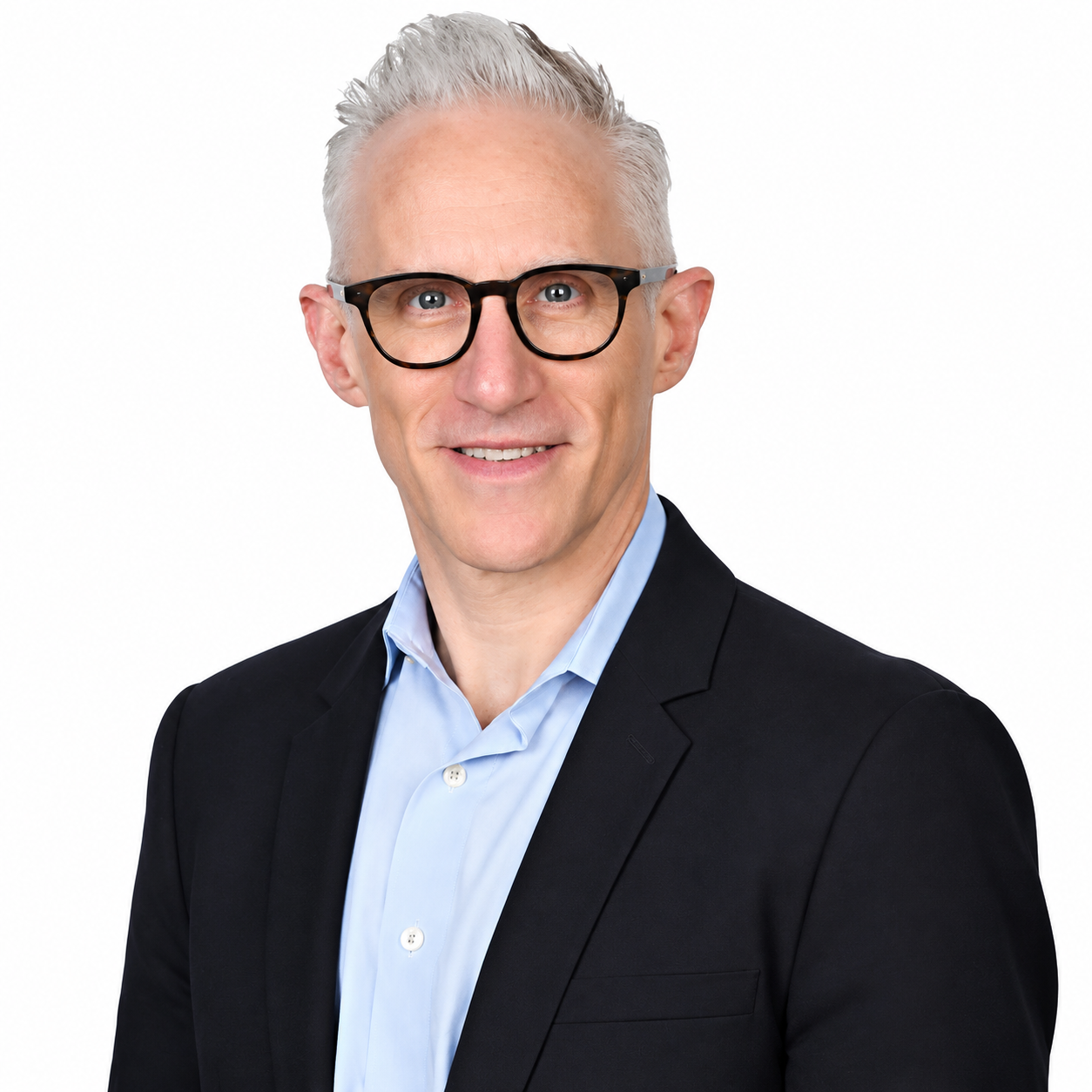 A light-skinned man in his 60s with short gray hair, blue eyes, and glasses, is wearing a light blue shirt and a blue blazer.