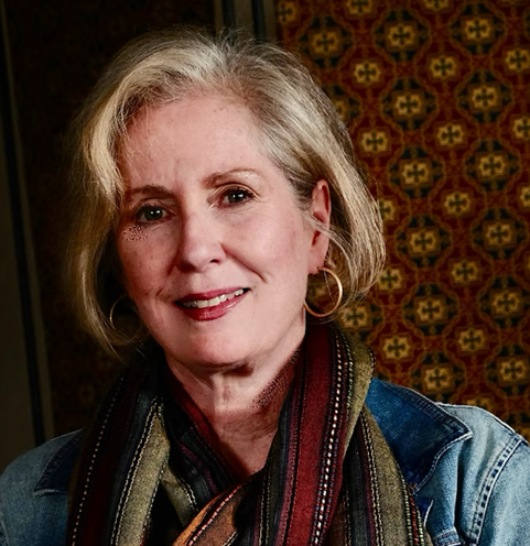 Kathryn Grant is a light-skinned woman who is in her 40s. She has blonde hair and dark eyes, and is wearing earrings, a multi-colored scarf, and a jean jacket.