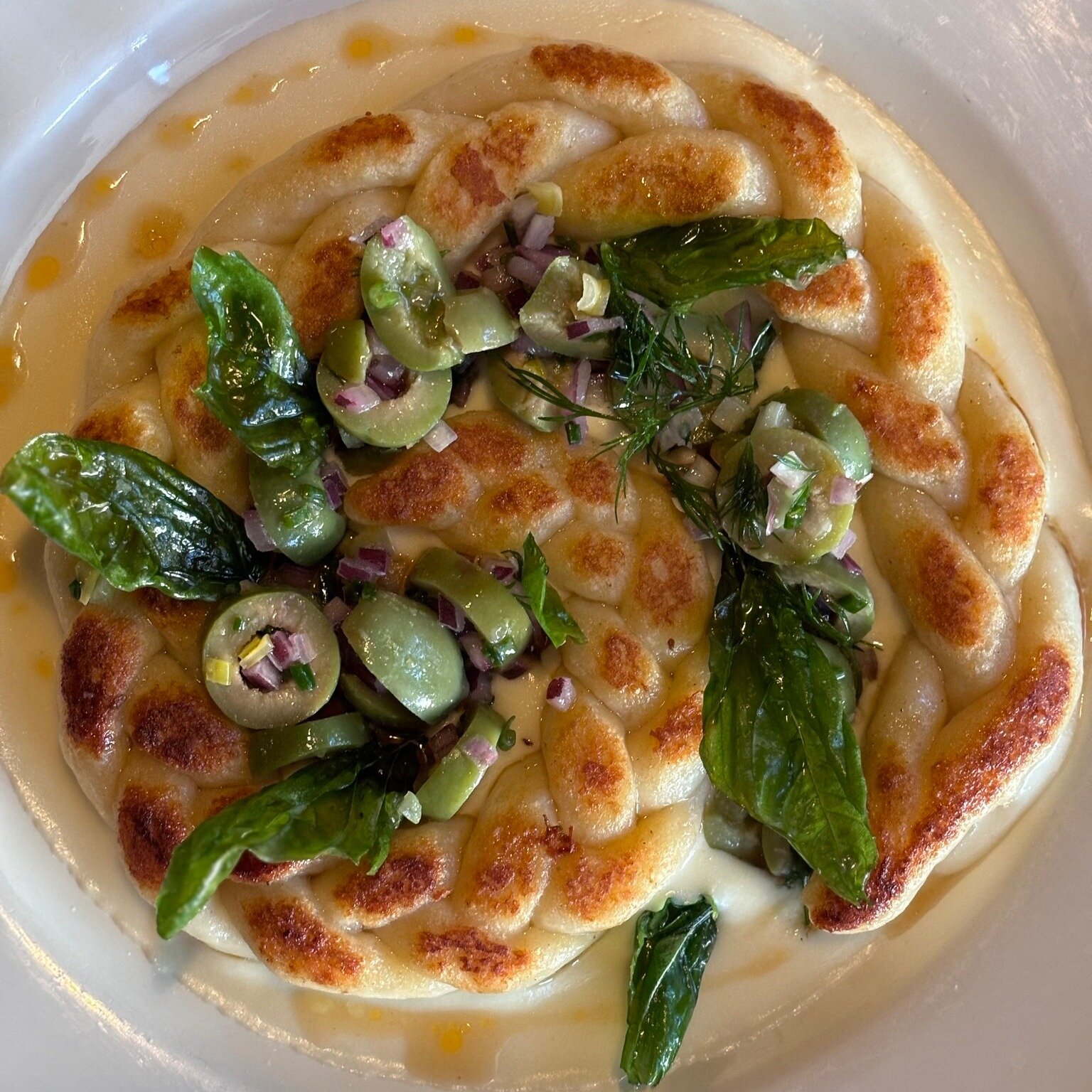 Thanks for everyone's great guesses! Meet Ella's latest creation...

gnocchi braid in a pool of ch&egrave;vre fondue, castelvetrano olive salad, crispy fried basil leaves and Calabrian chili oil $26