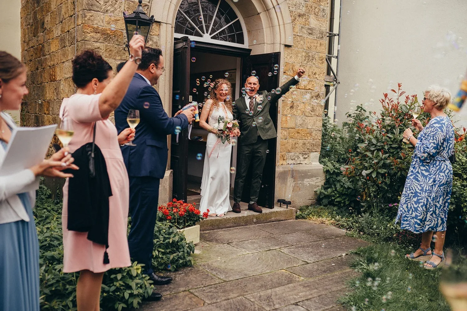 Brautpaar tritt aus der Protestantischen Kirche, Gäste jubeln mit Sektgläsern bei einer Hochzeit in Deidesheim