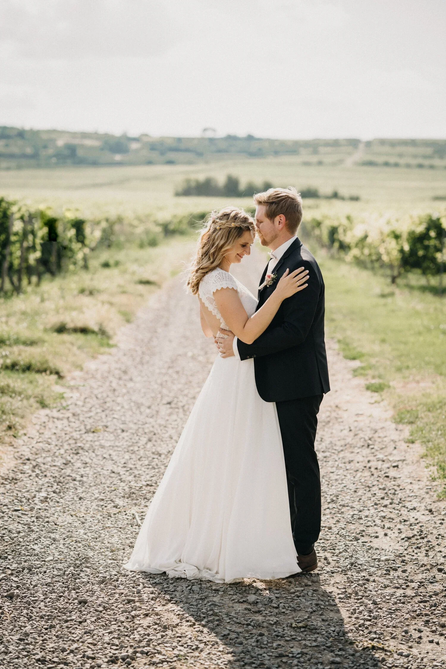 Hochzeitspaar umarmt sich auf einem Weg zwischen Weinbergen in der Pfalz