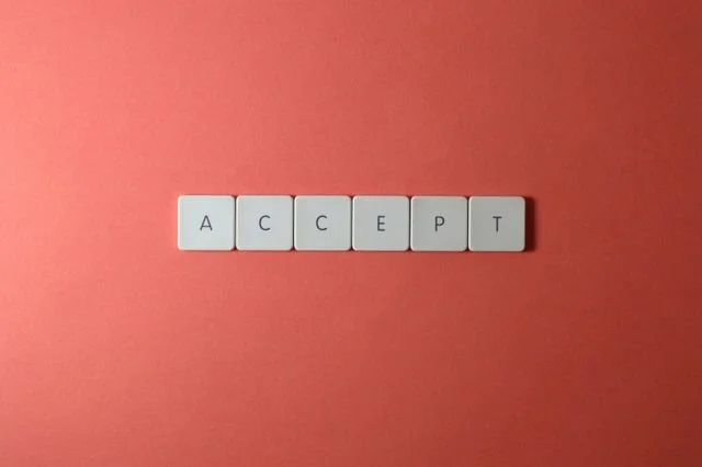 Small, square letter tiles spelling ACCEPT with plain, orange background