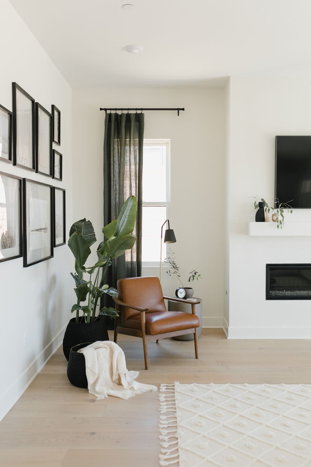 Warm and cozy corner of living room with brown leather chair, green curtains, art and plants.