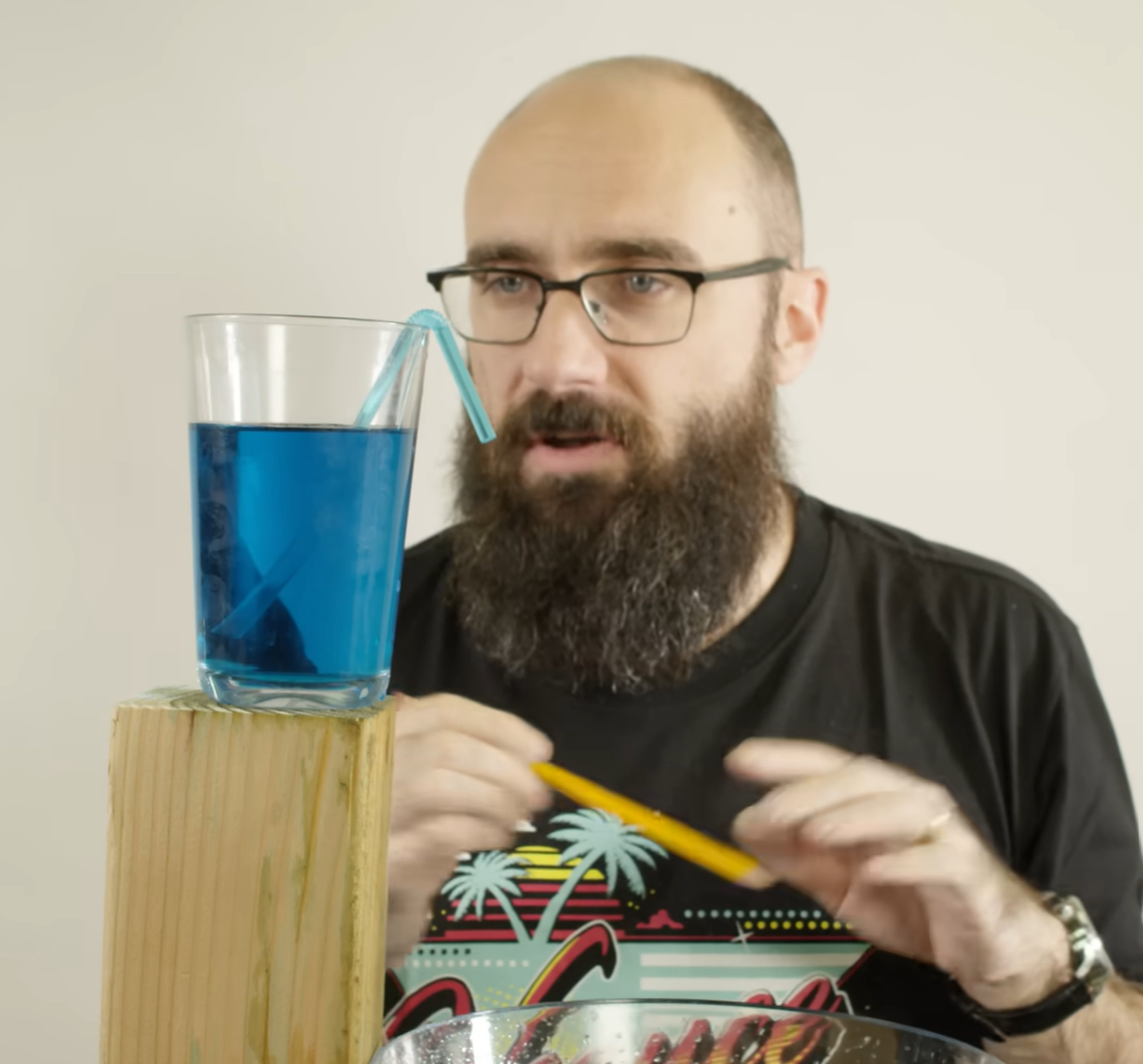a man lookin gat a cup filled with blue liquid and a straw