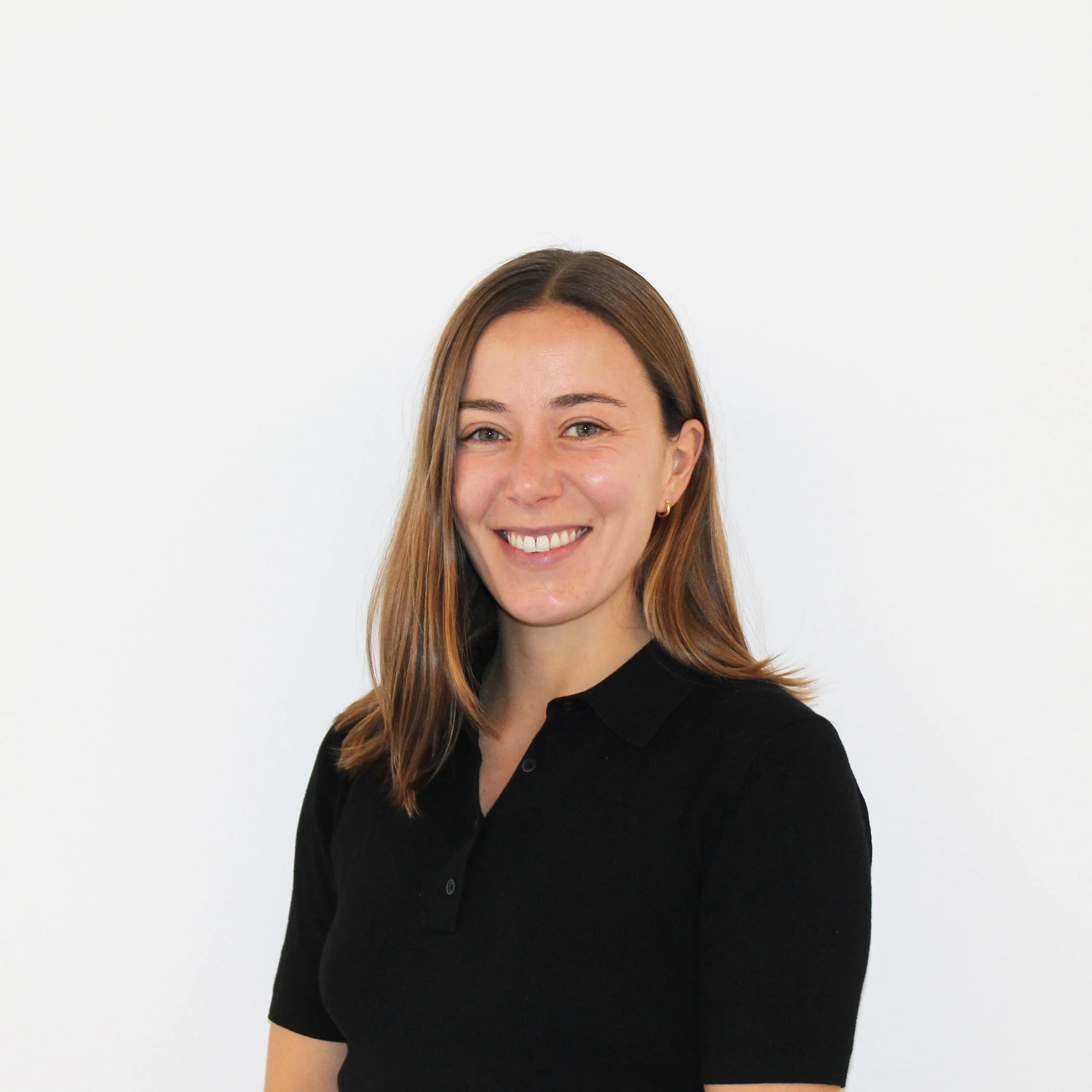 Portrait of a woman with shoulder-length brown hair, wearing a black polo shirt, smiling, standing against a white background.